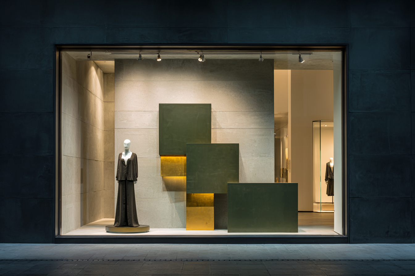 Display window showcasing a mannequin dressed in dark clothing, with abstract green and gold geometric art inside a modern, minimalist storefront.