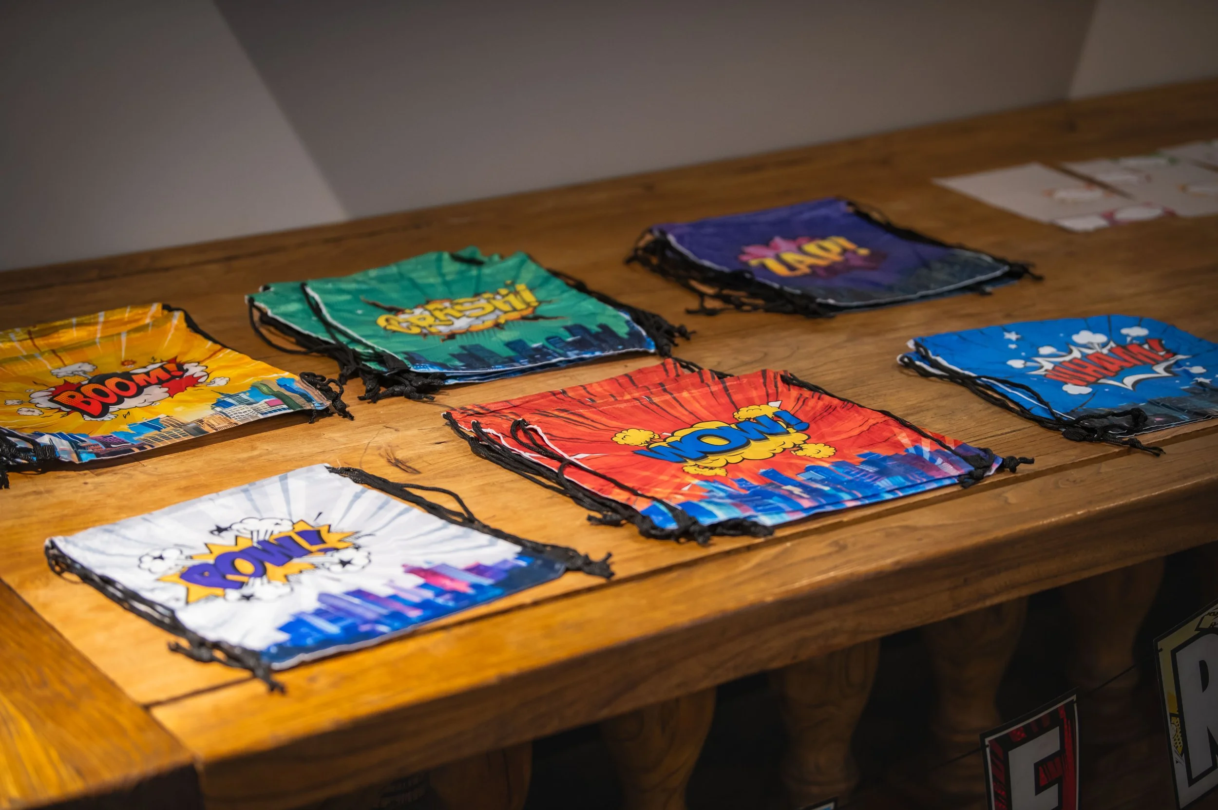Colorful face masks with comic book style words like 'BOOM,' 'WOW,' and 'ZAP' laid out on a wooden table.