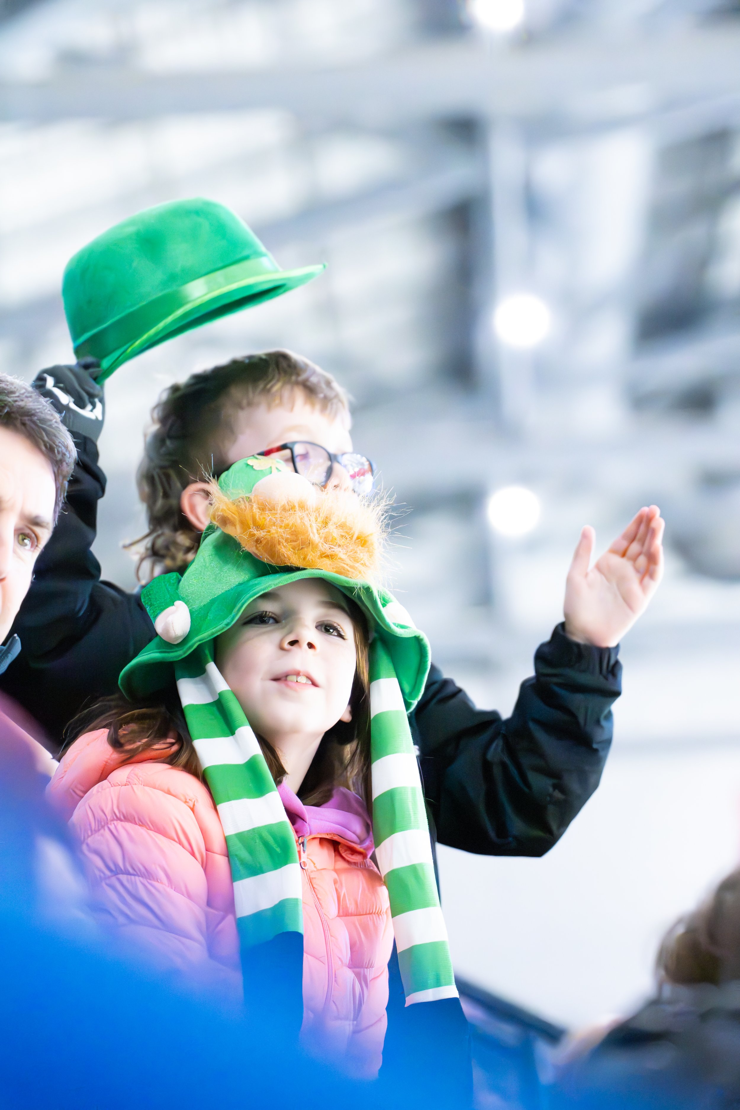 Children wearing festive hats, including a girl with a leprechaun hat, in an indoor setting.