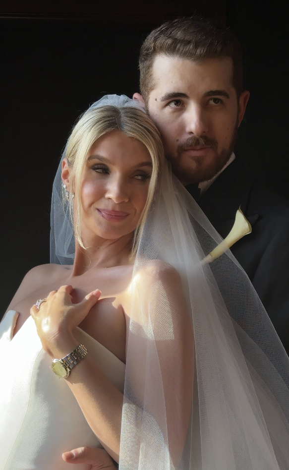 A bride and groom posing for a wedding photo, with the bride holding her hand on her shoulder and wearing a veil, while the groom stands behind her in a tuxedo. Forever After, Instantly Wedding Content Creator in Texas.