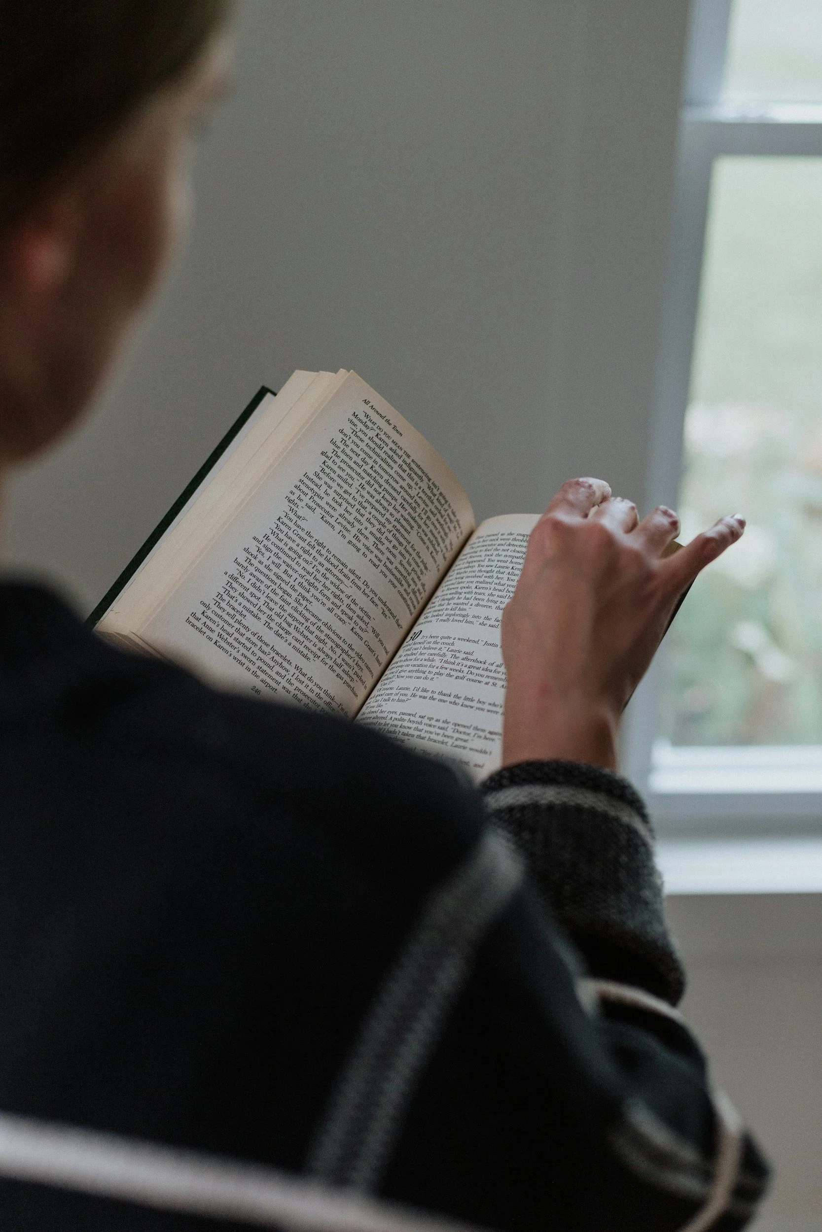 Person reading a book near a window with natural light.