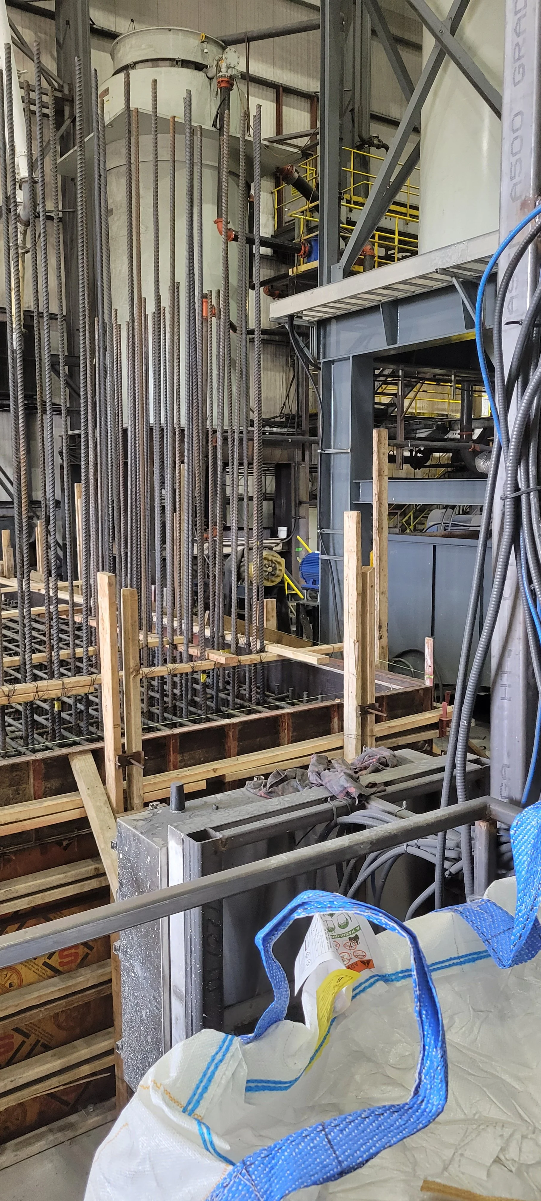 Construction site with steel rebar, wooden formwork, and construction tools, indicating a building foundation in progress.