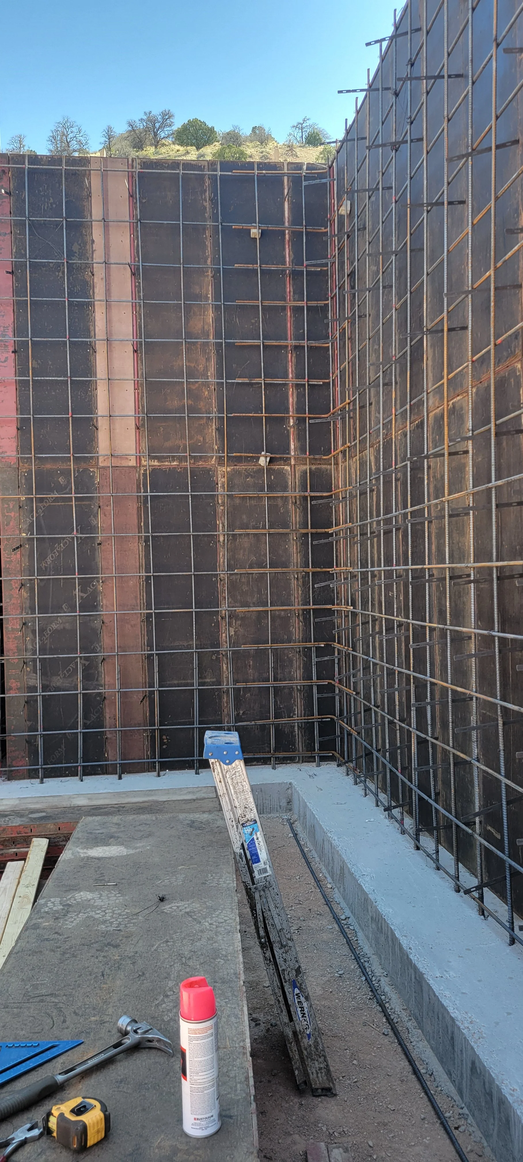 Construction site with rebar framework for a concrete wall and tools on a table in the foreground.