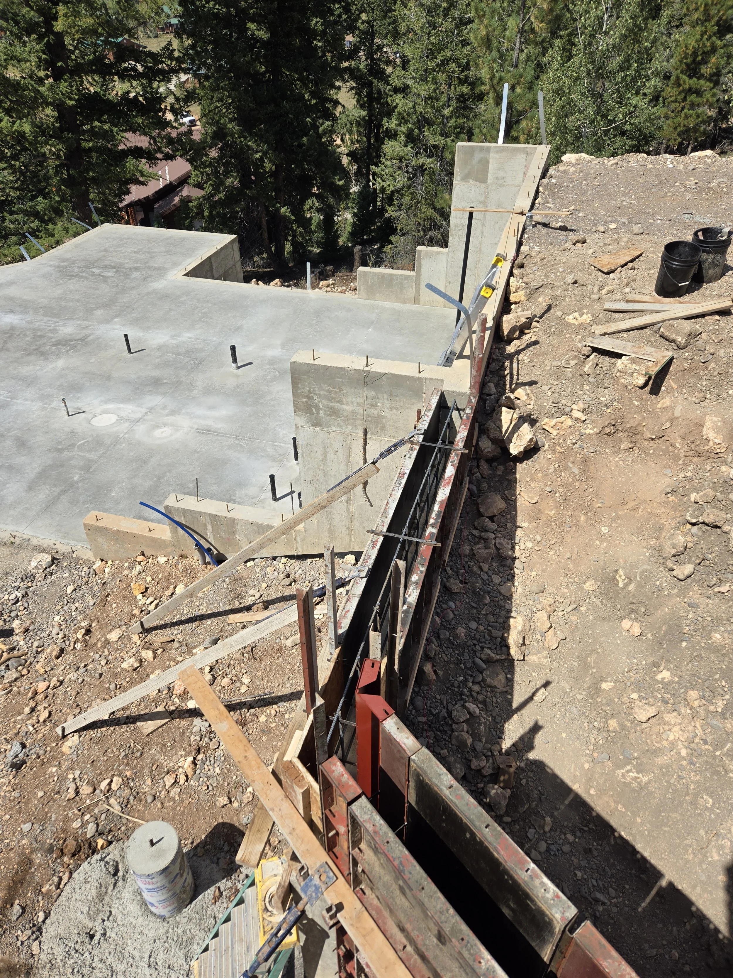 Concrete stairs being constructed on a hillside with wooden formwork and metal rebar, surrounded by dirt and construction tools.