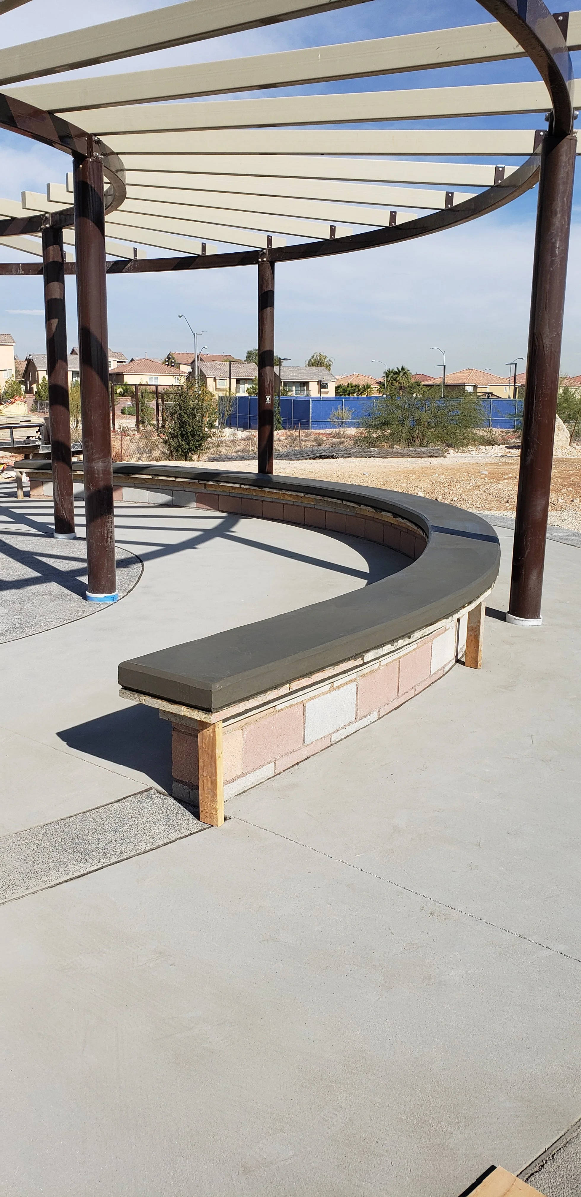 A curved concrete bench with wooden supports at an outdoor construction site.