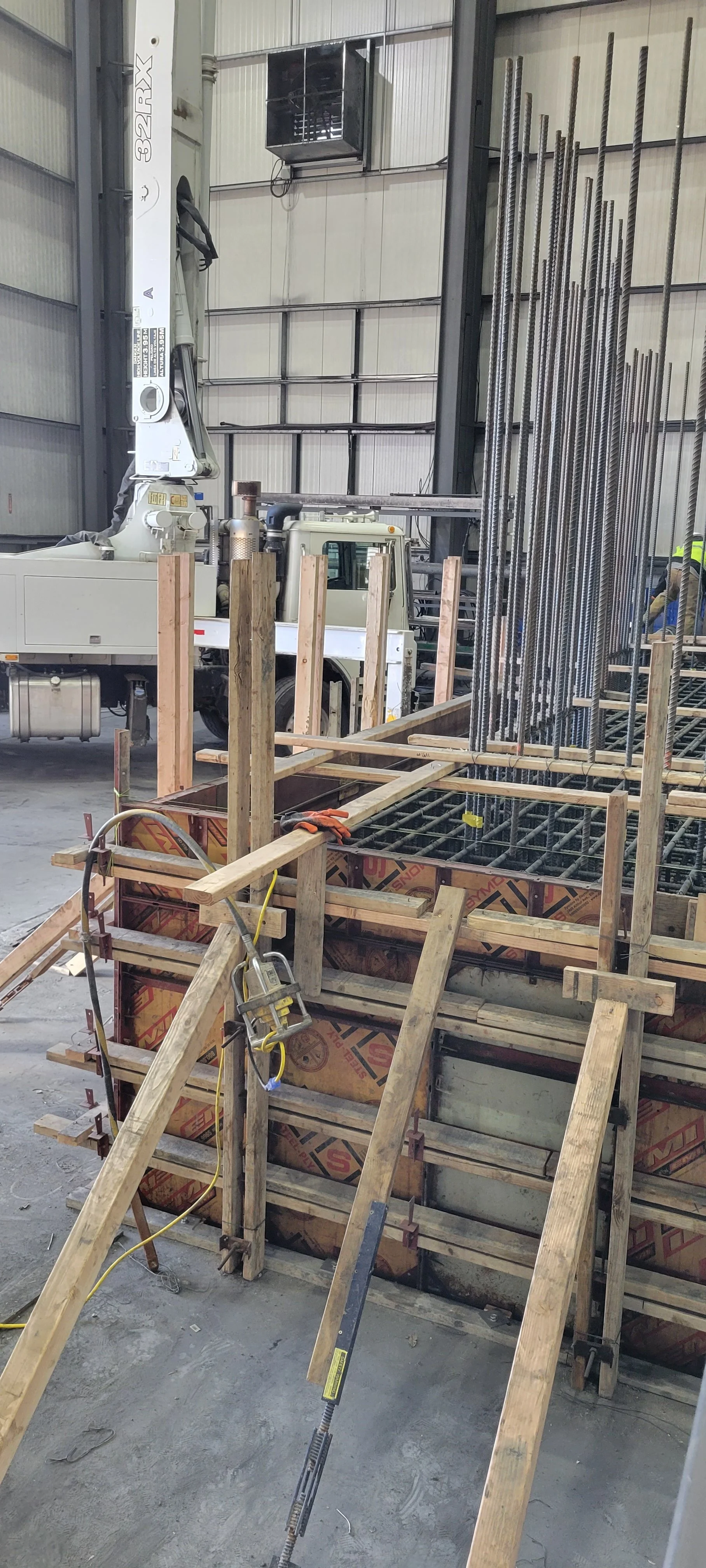 Construction site with steel rebar, wooden formwork, and a crane inside a warehouse.