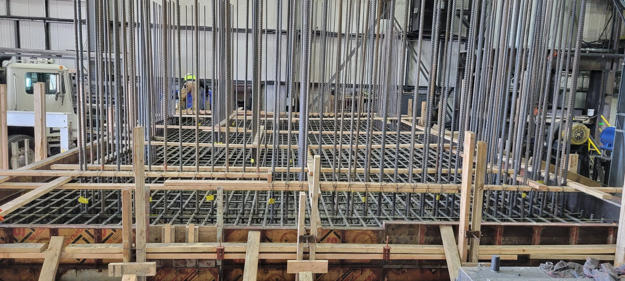 Construction site with rebar framework and wooden formwork, workers in safety gear working on a building foundation.