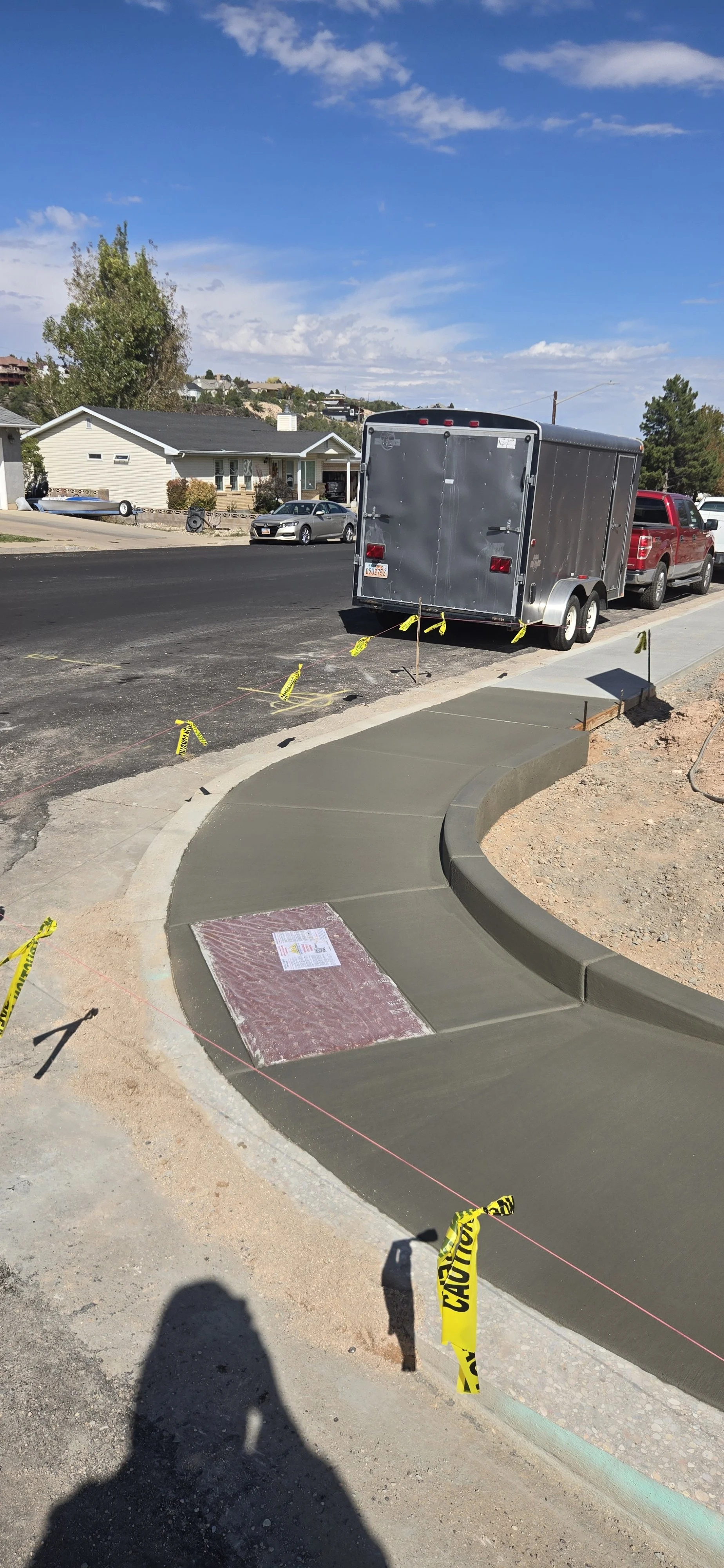 Newly poured concrete sidewalk with curb, sectioned off with yellow caution tape at a construction site on a residential street.