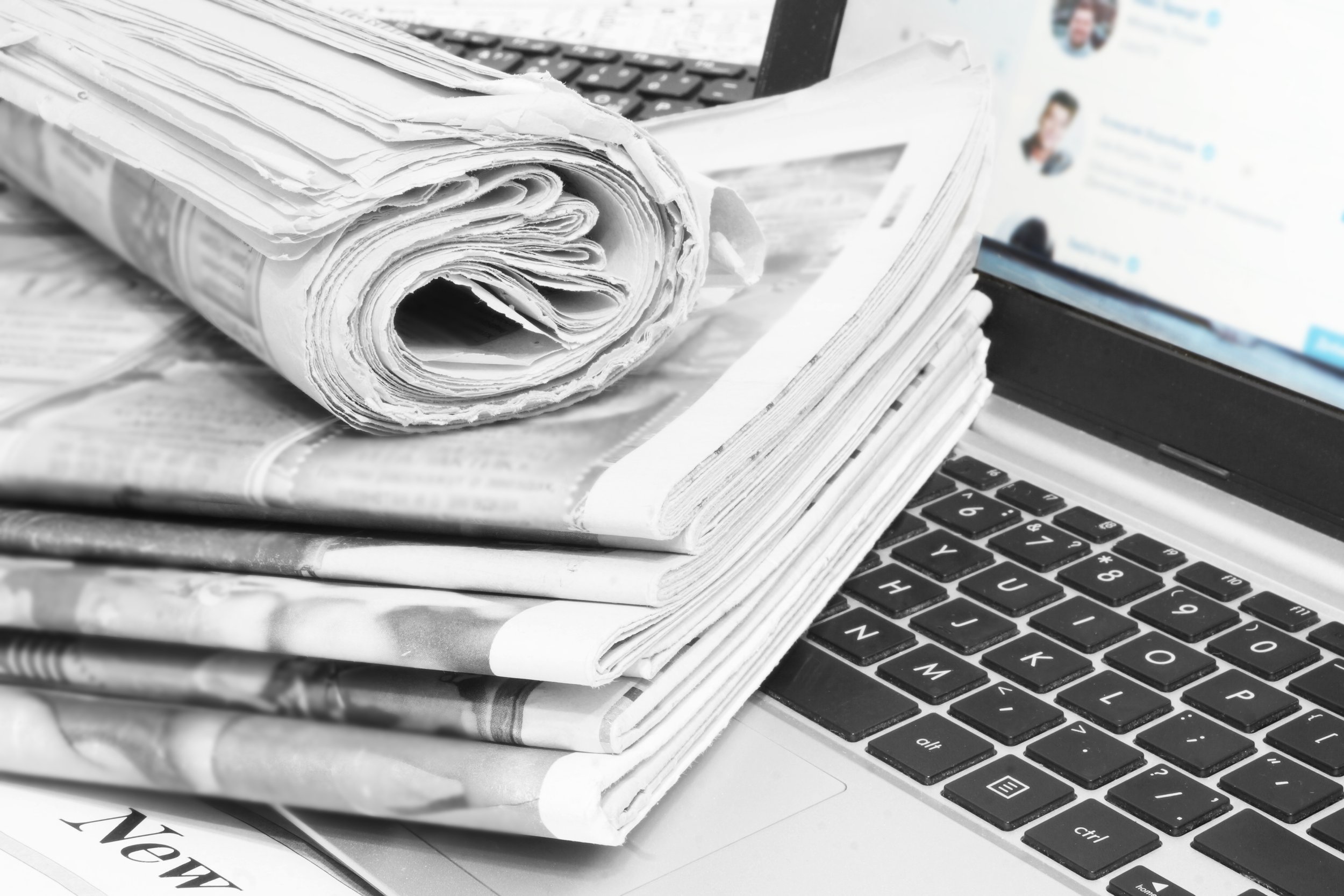 Stack of newspapers, a laptop keyboard, and a computer screen displaying social media profiles.