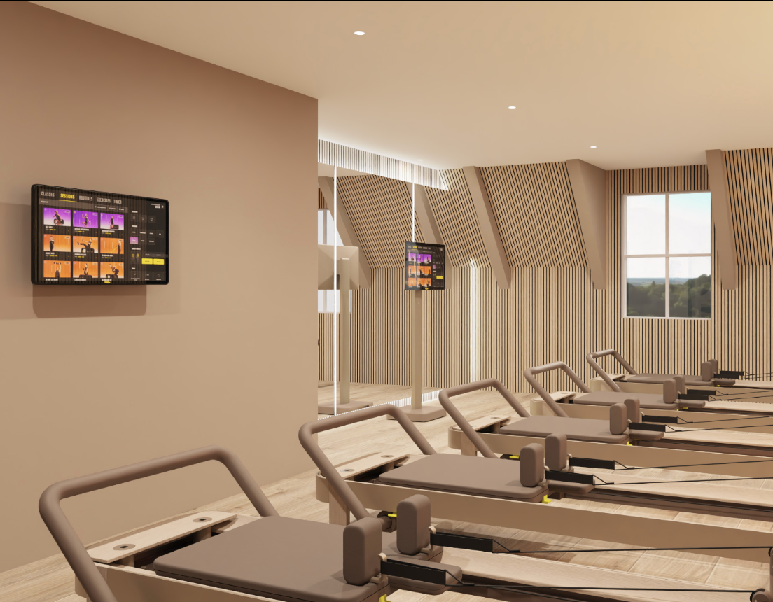 Indoor fitness studio with rowing machines lined up facing the wall, digital screens on the wall, wooden slat wall decor, and a large window showing outdoor landscape.
