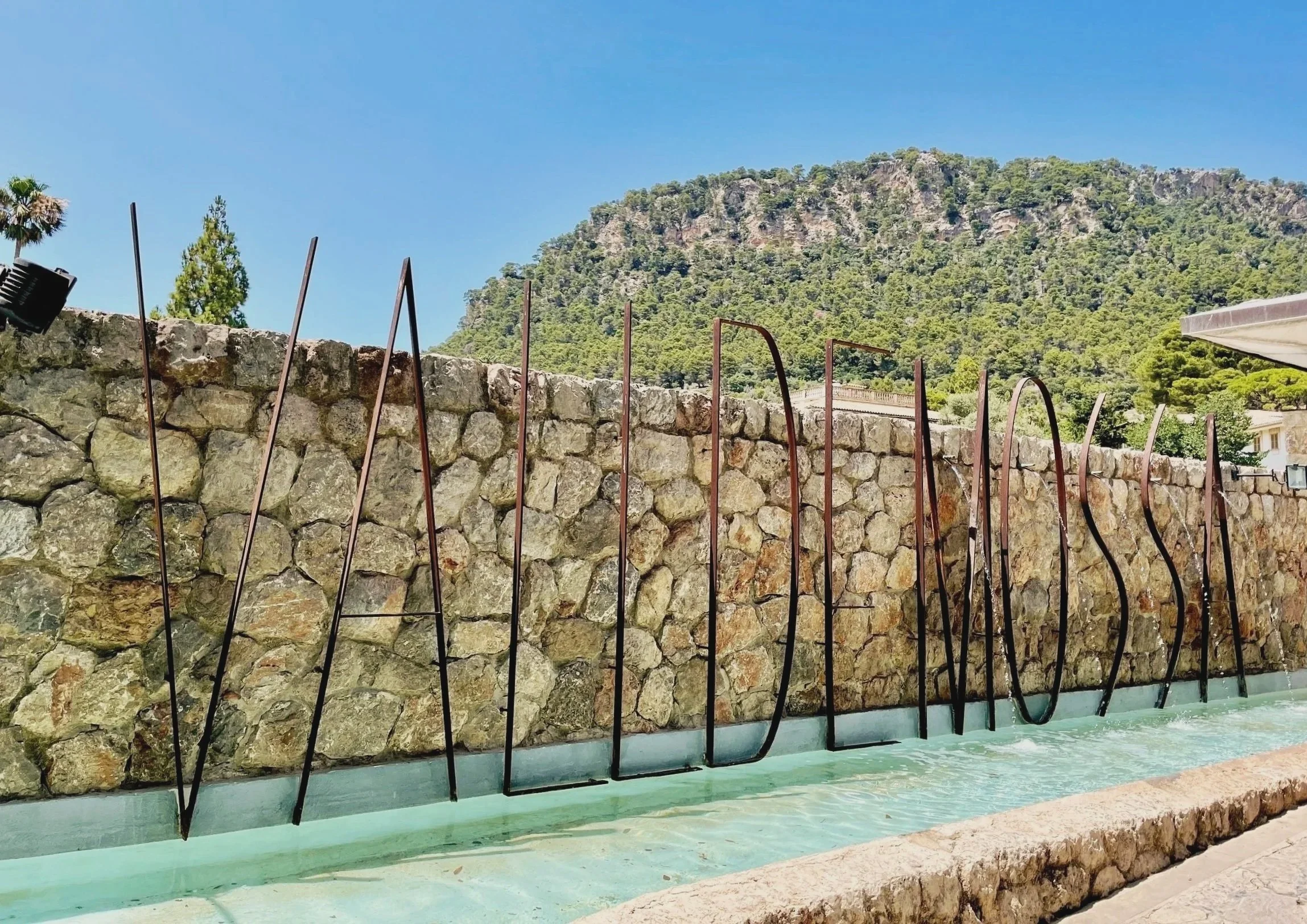 The large lettered Valldemossa sign and fountain witht he Tramuntana mountains in the background