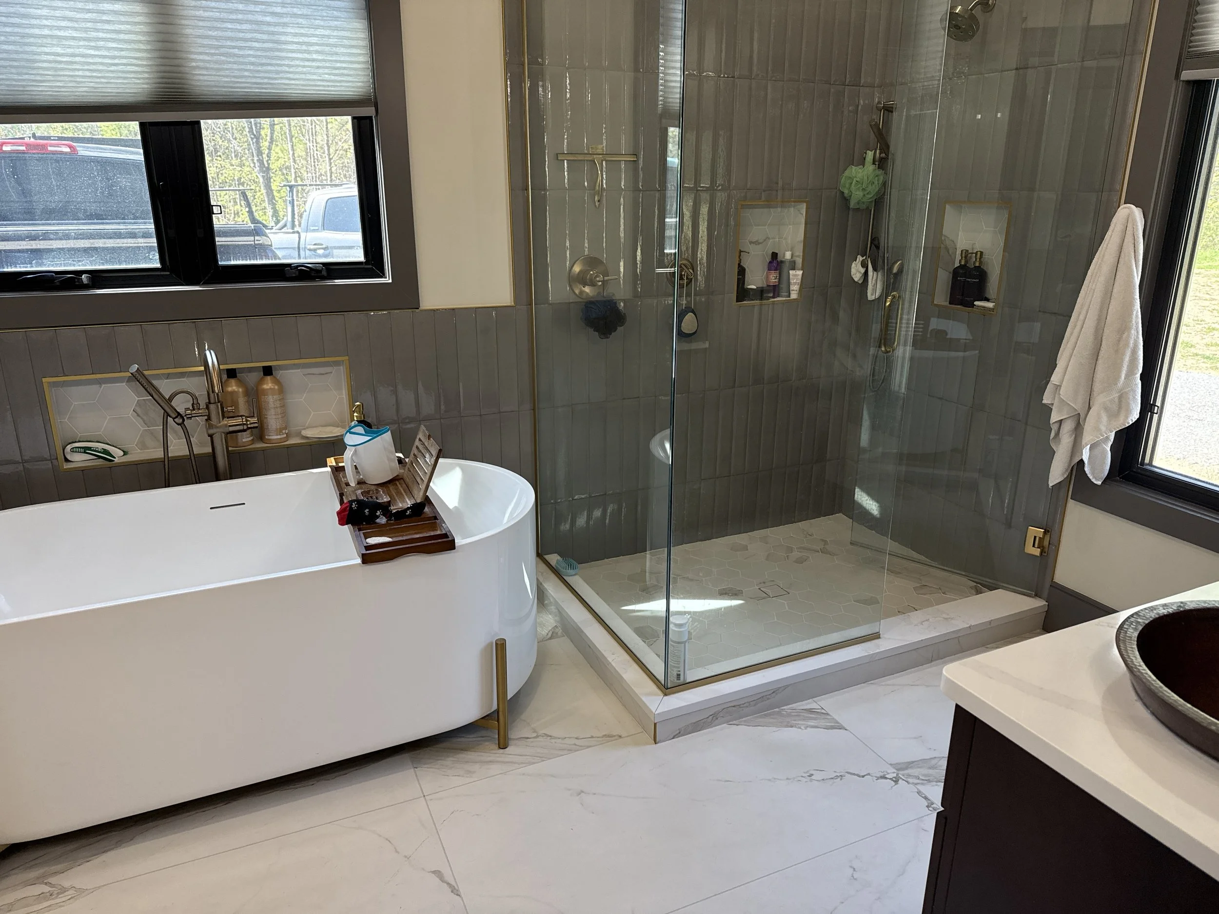 Custom home master bathroom build in Ringgold GA featuring large format heated white floor tile, a freestanding white soaking tub, an integrated glass-enclosed custom tile shower, custom his-and-hers vanities, and expansive natural light windows.