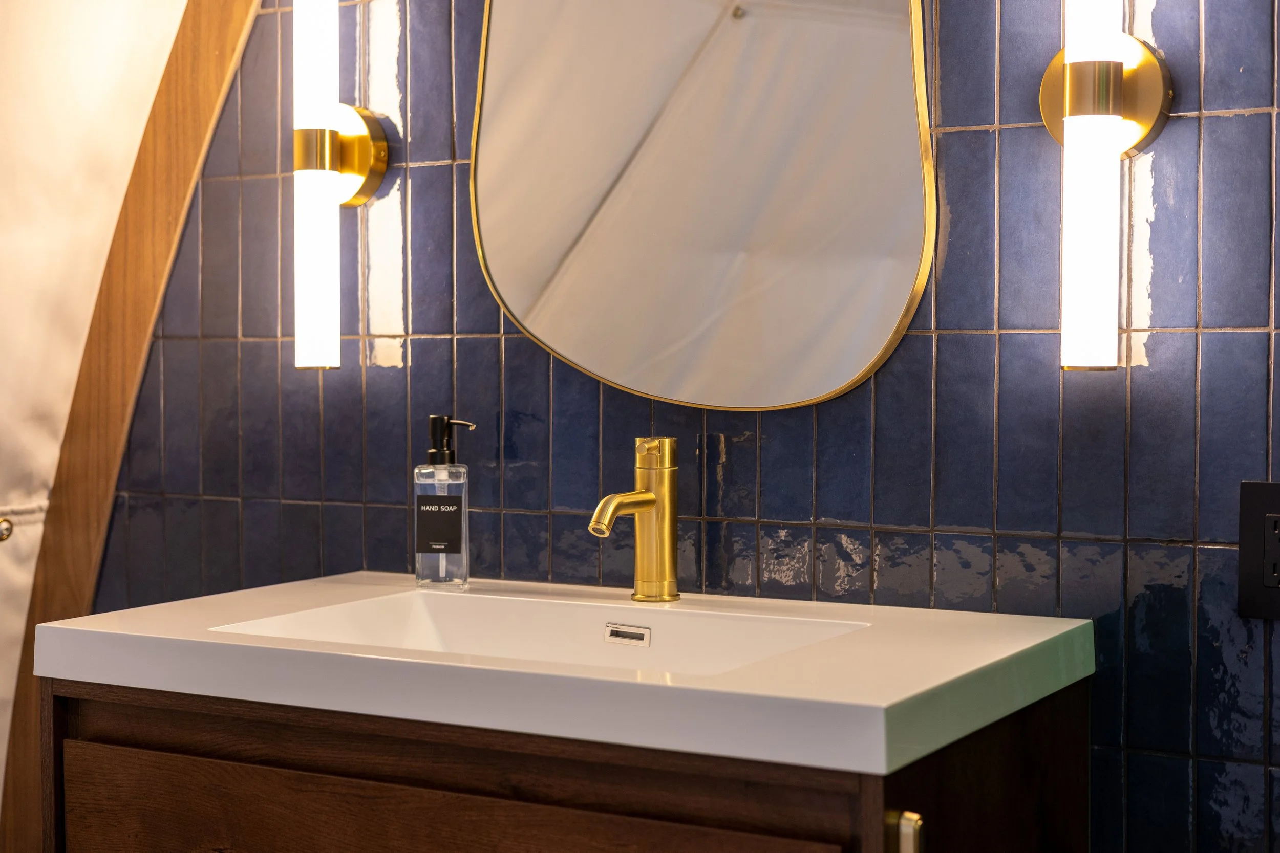 Bespoke bathroom remodel at a luxury retreat near Trenton GA, featuring custom hand-laid blue wall tile spanning all surfaces, a custom floating vanity sink, gold fixtures, matching vanity mirror, and premium custom-hung pendant accent lighting.
