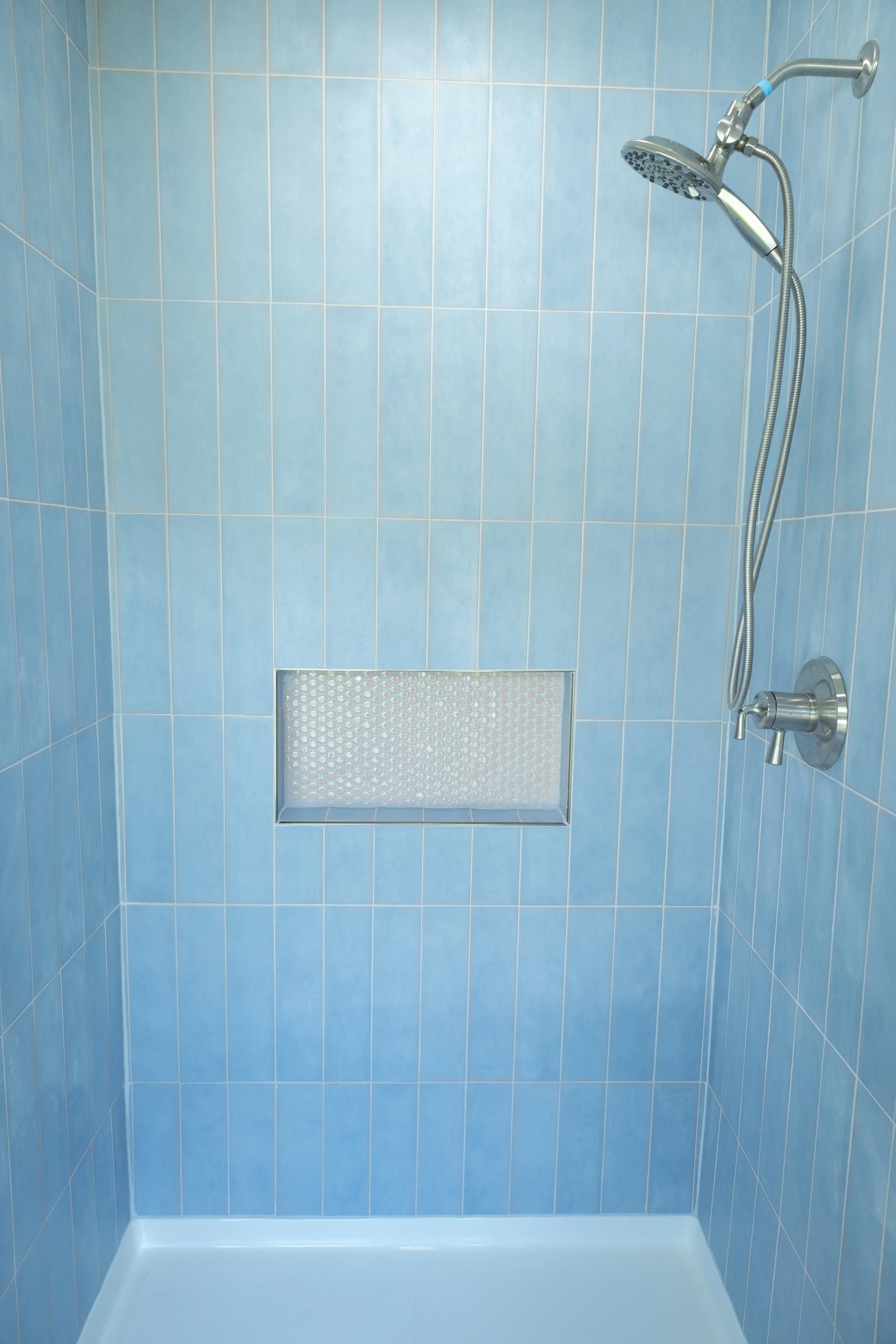 Custom residential shower remodel in Dayton TN displaying premium blue wall tile layouts, integrated white accent tile cutout storage shelves, silver fixtures, and precision waterproofing membranes.
