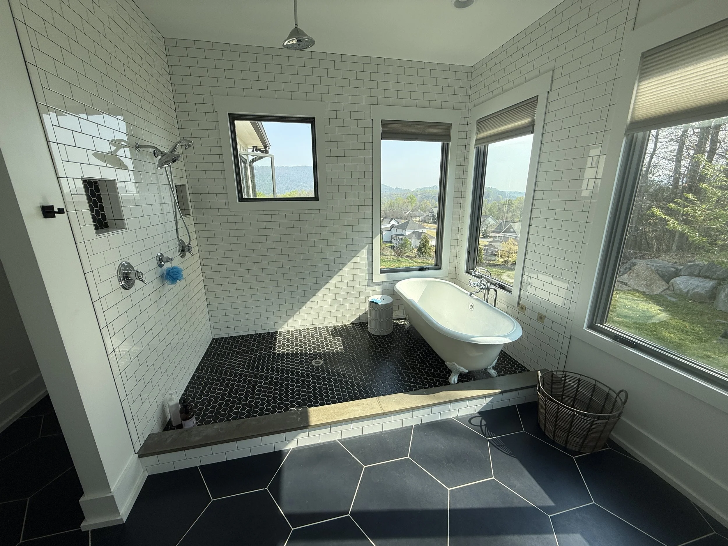 Custom bathroom remodel near Black Creek Golf Club in Chattanooga TN, showcasing a clawfoot historic style soaking tub inside a glass-enclosed shower wet room, white subway tile walls with premium black tile flooring and natural light windows. 