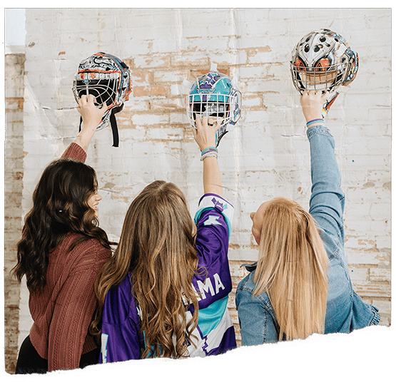 Three woman holding up hockey helmets