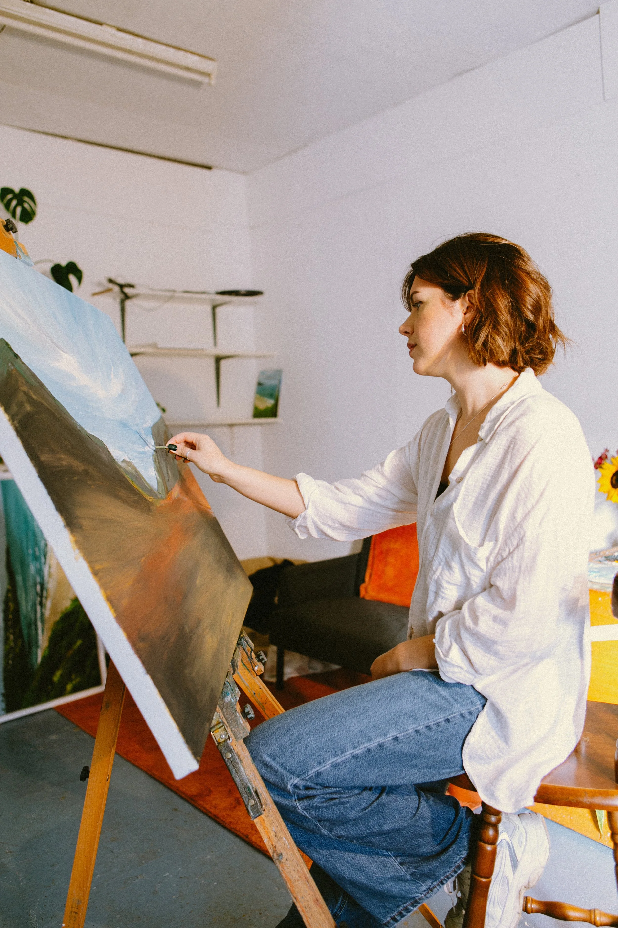 A woman painting a landscape scene on a canvas in a cozy indoor studio.