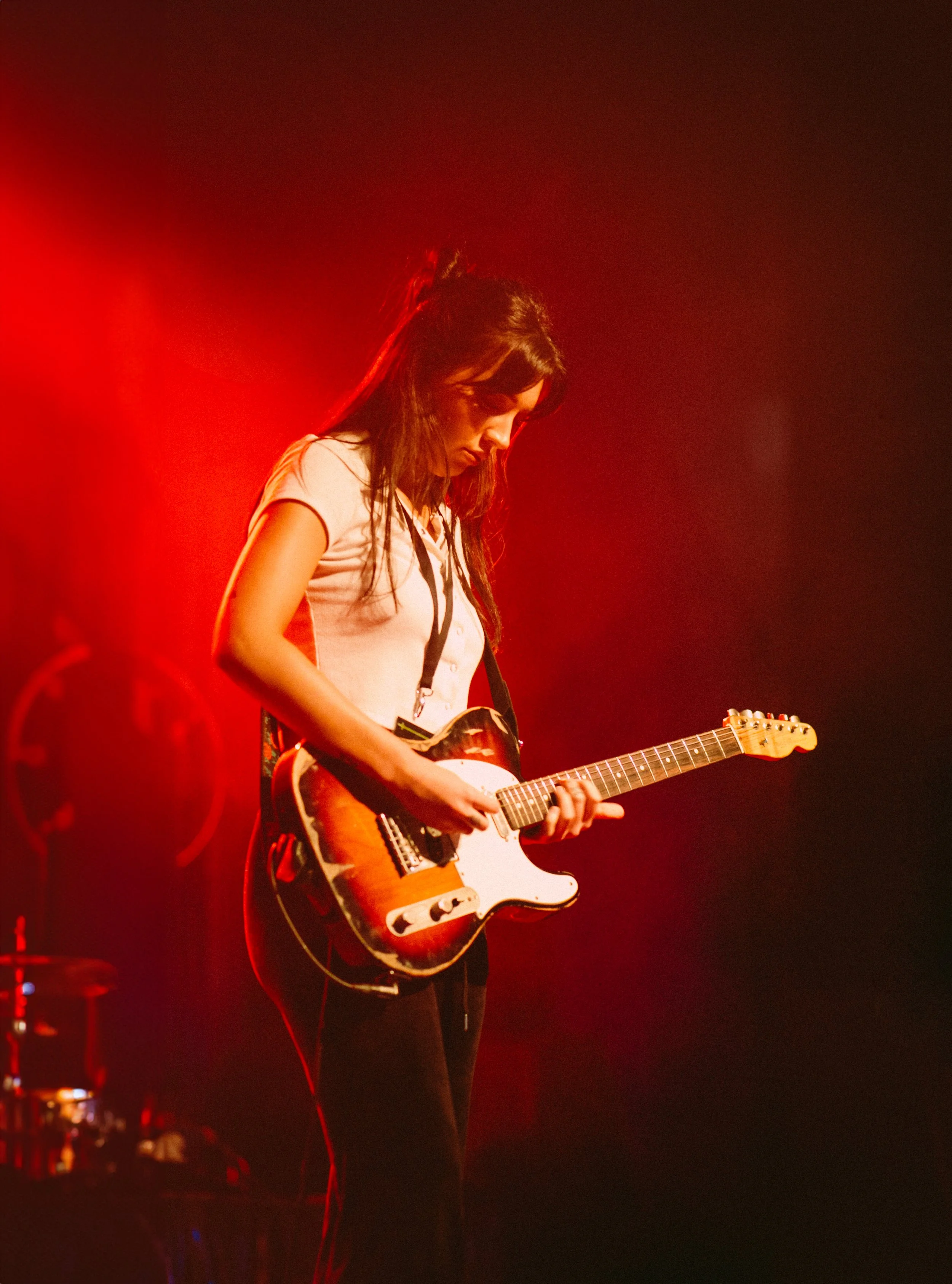 A woman playing an electric guitar on stage with red lighting.