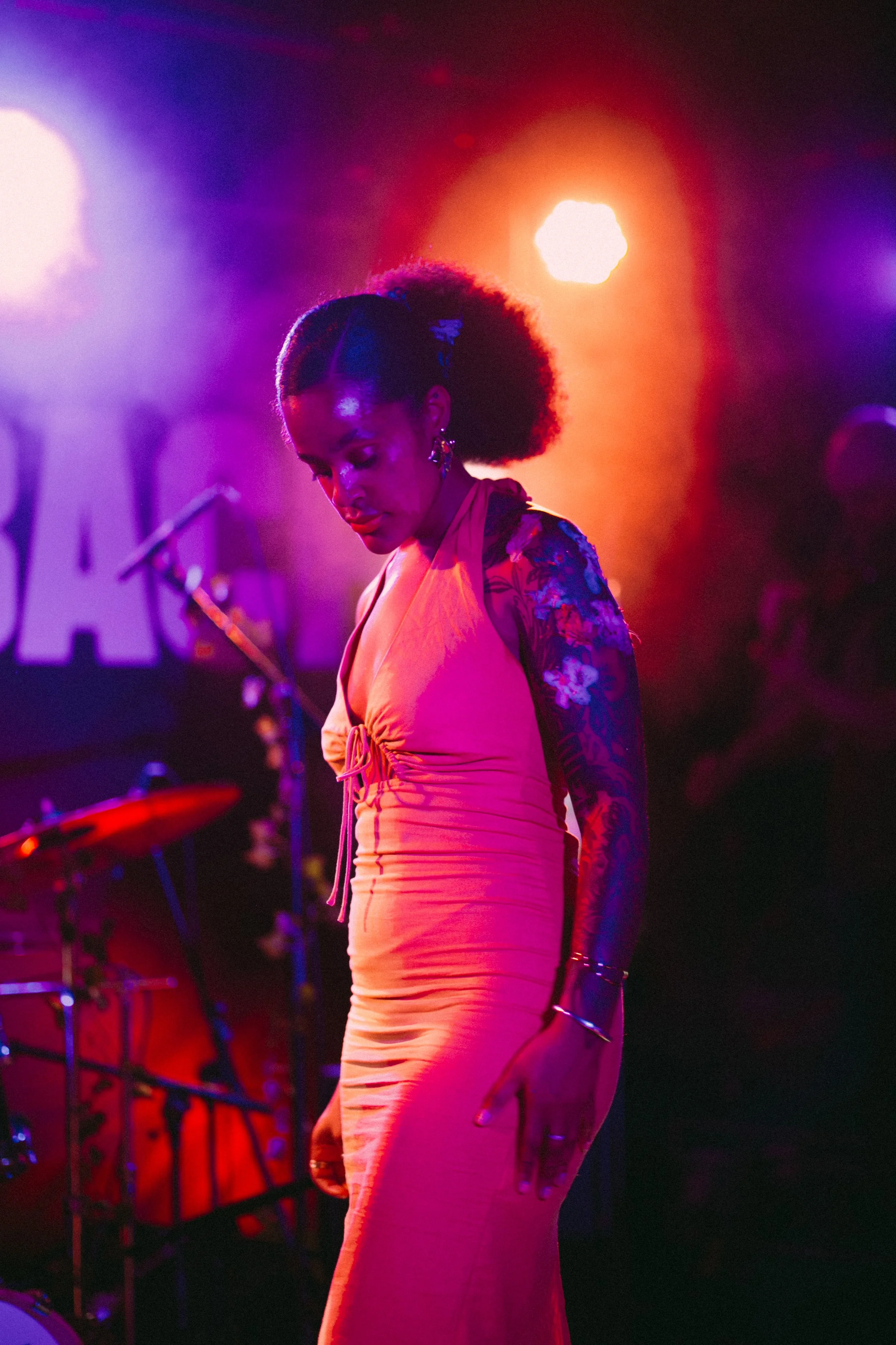A woman singing on stage with colorful lighting and musical instruments in the background.