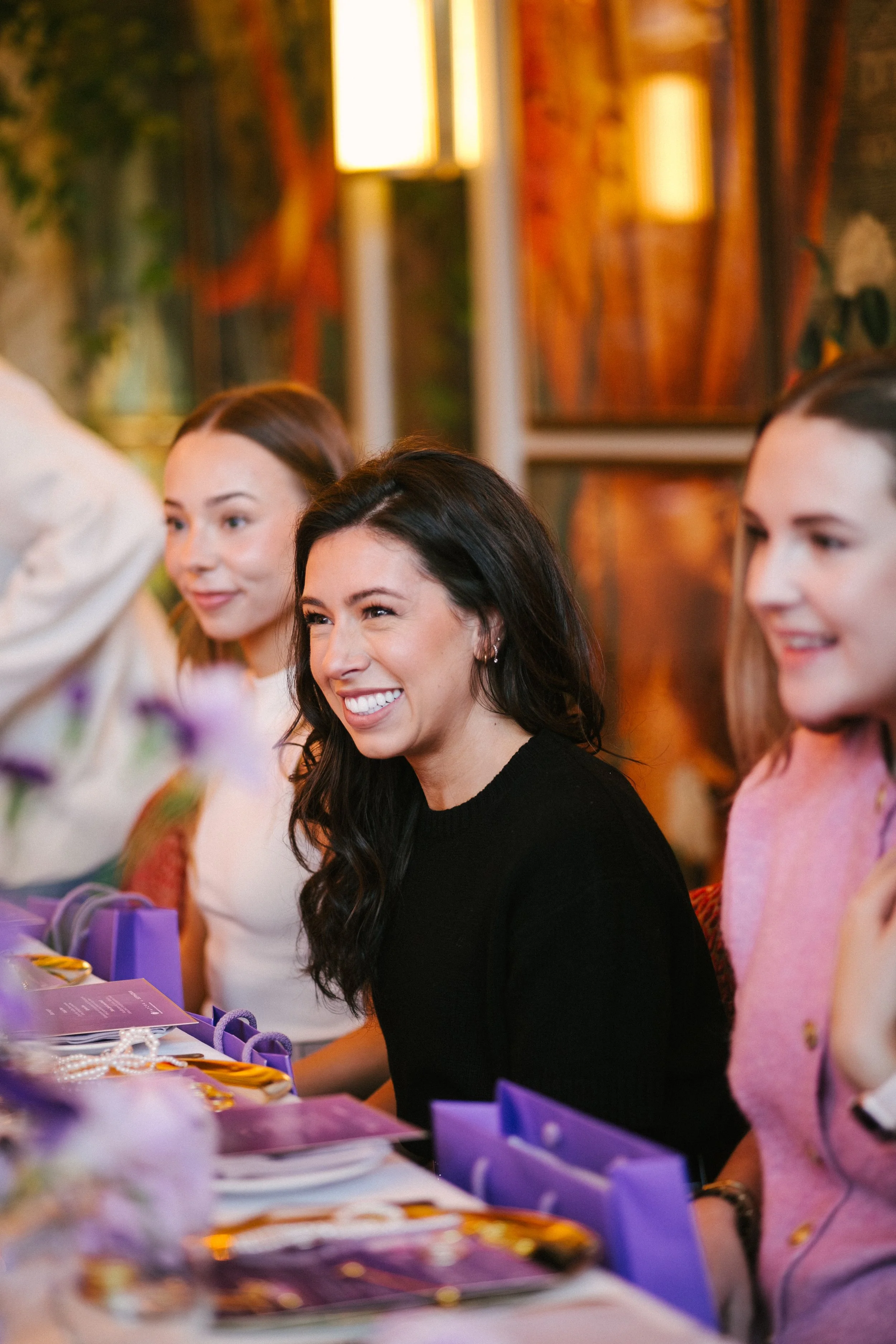 Women sitting at a table, smiling, at a social gathering or celebration.