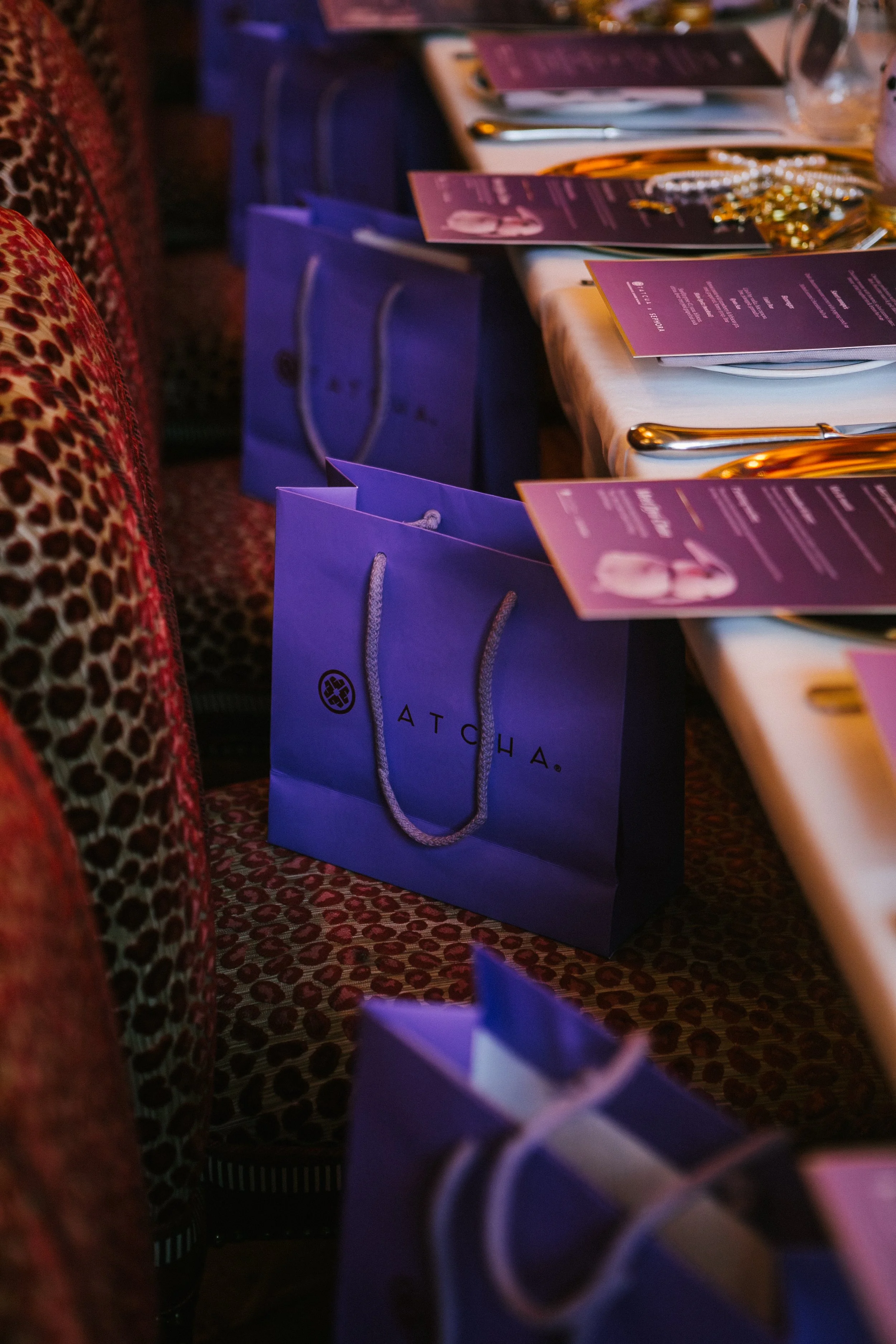 Purple gift bags with the "Alocha" logo on the table along with event programs and jewelry accessories.