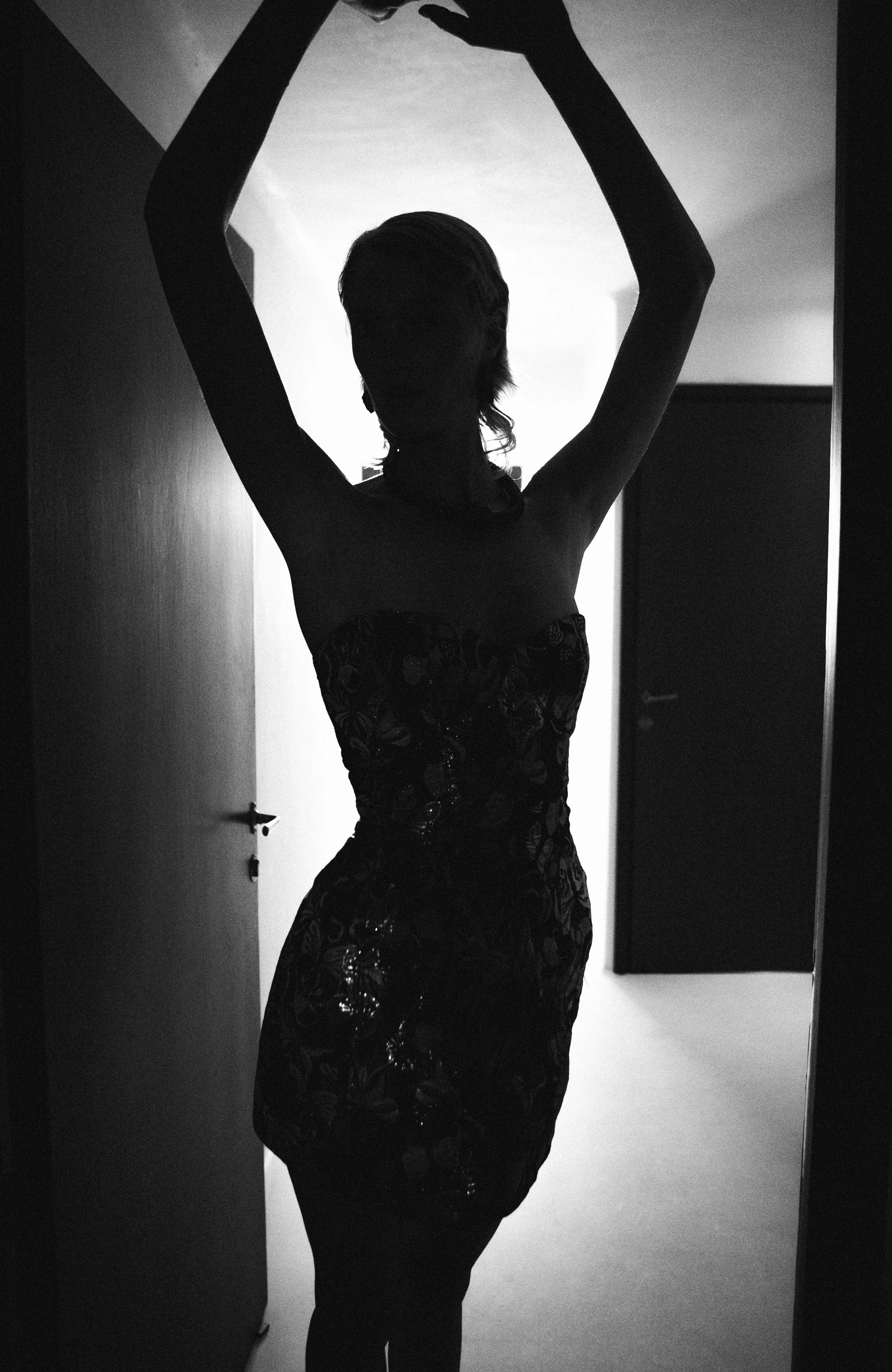 Silhouette of a woman with arms raised, standing in a doorway with light behind her, creating a silhouetted effect.