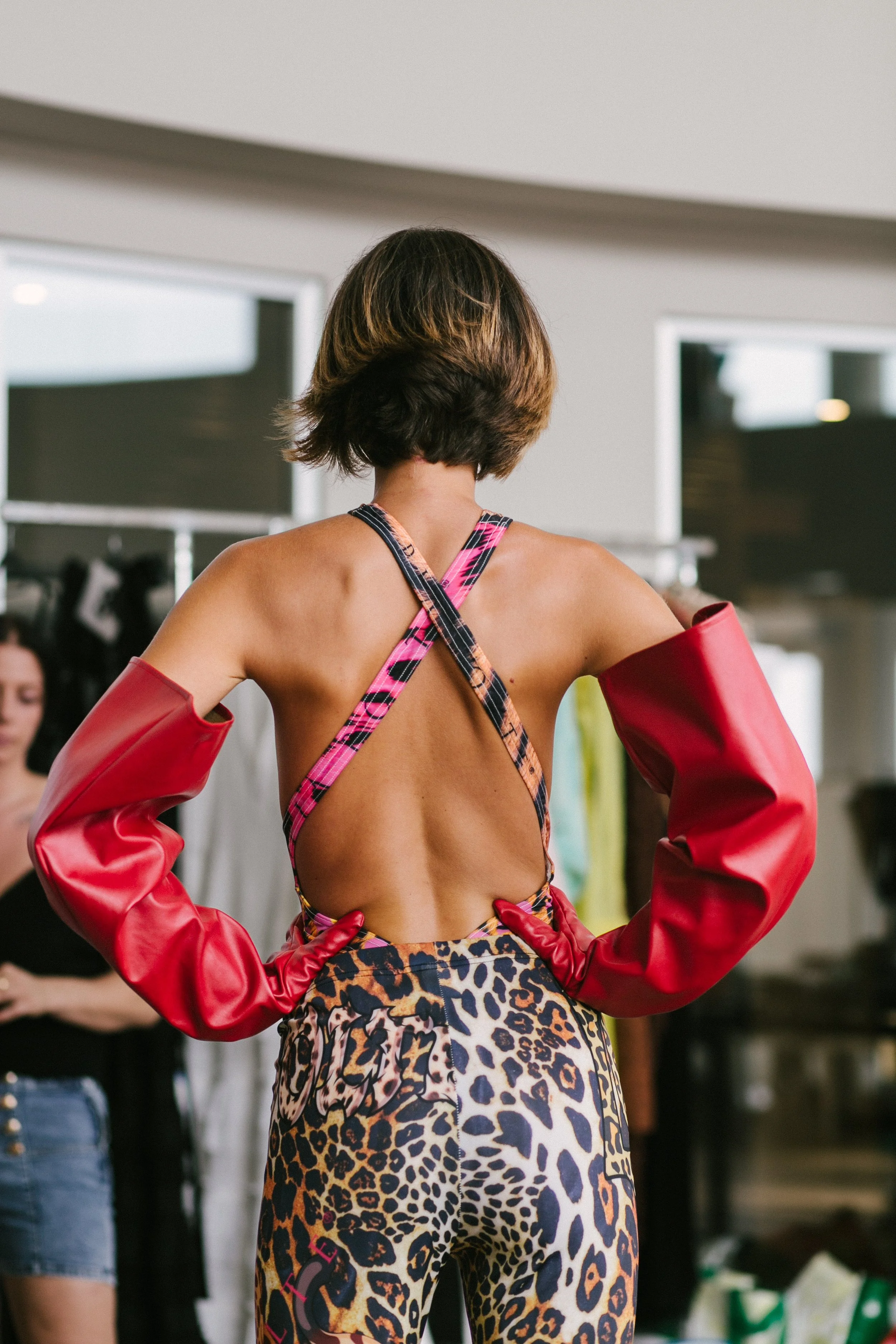 Back view of a woman wearing a colorful animal print outfit with a cut-out back, red sleeves, and crossed straps in a fashion setting.