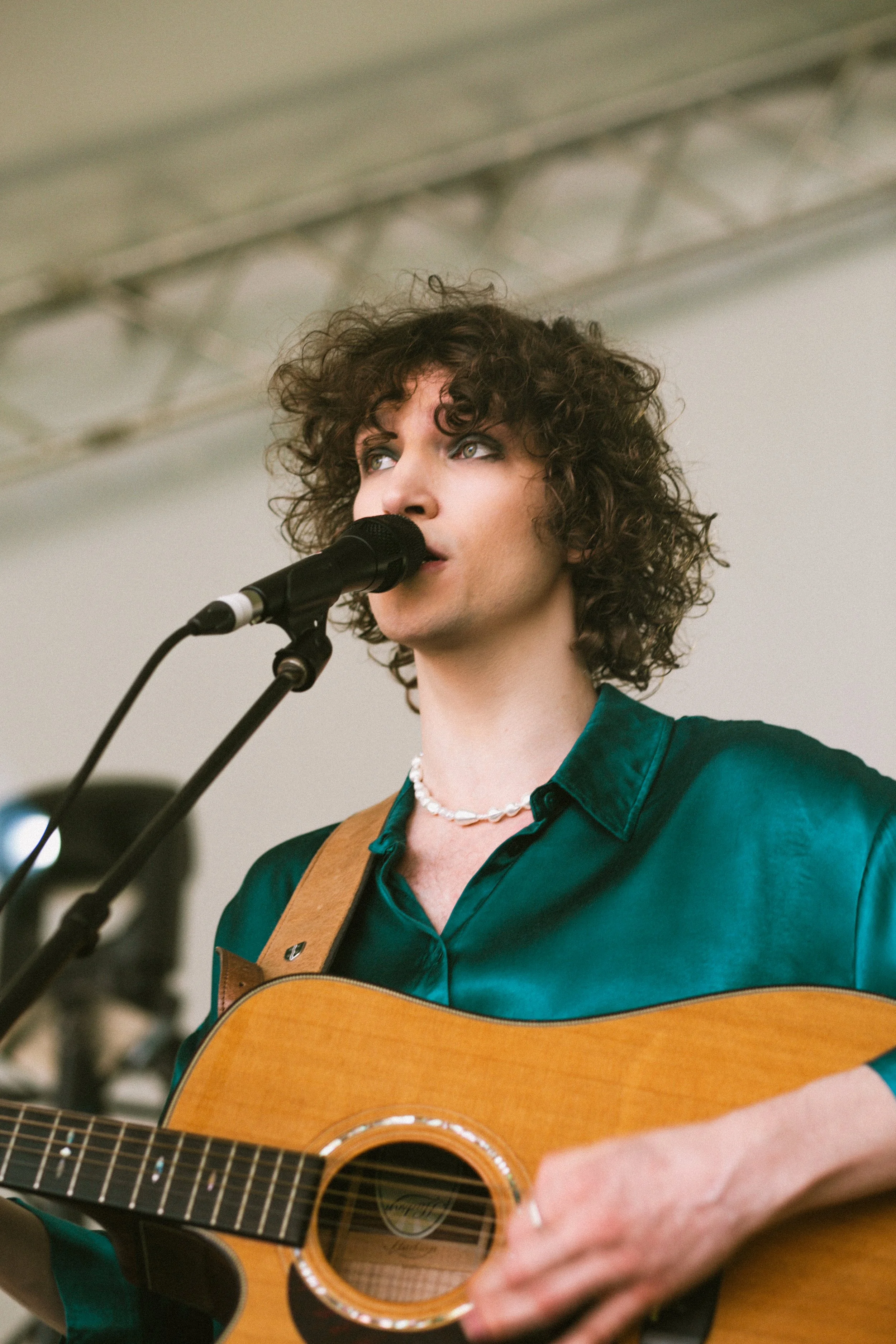 A person with curly hair singing into a microphone while playing an acoustic guitar.
