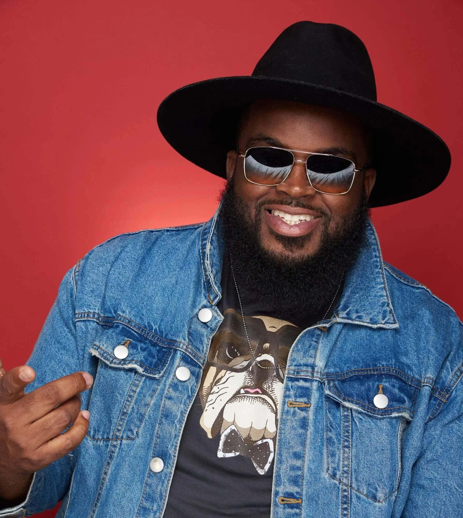 red background man in jean jacket graphic tee sunglasses and black hat