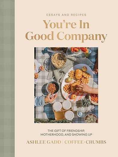 Book cover titled "You're In Good Company" by Ashlee Gadd, featuring a table with food and drinks, including waffles, grapes, a bowl of cereal, and coffee cups.