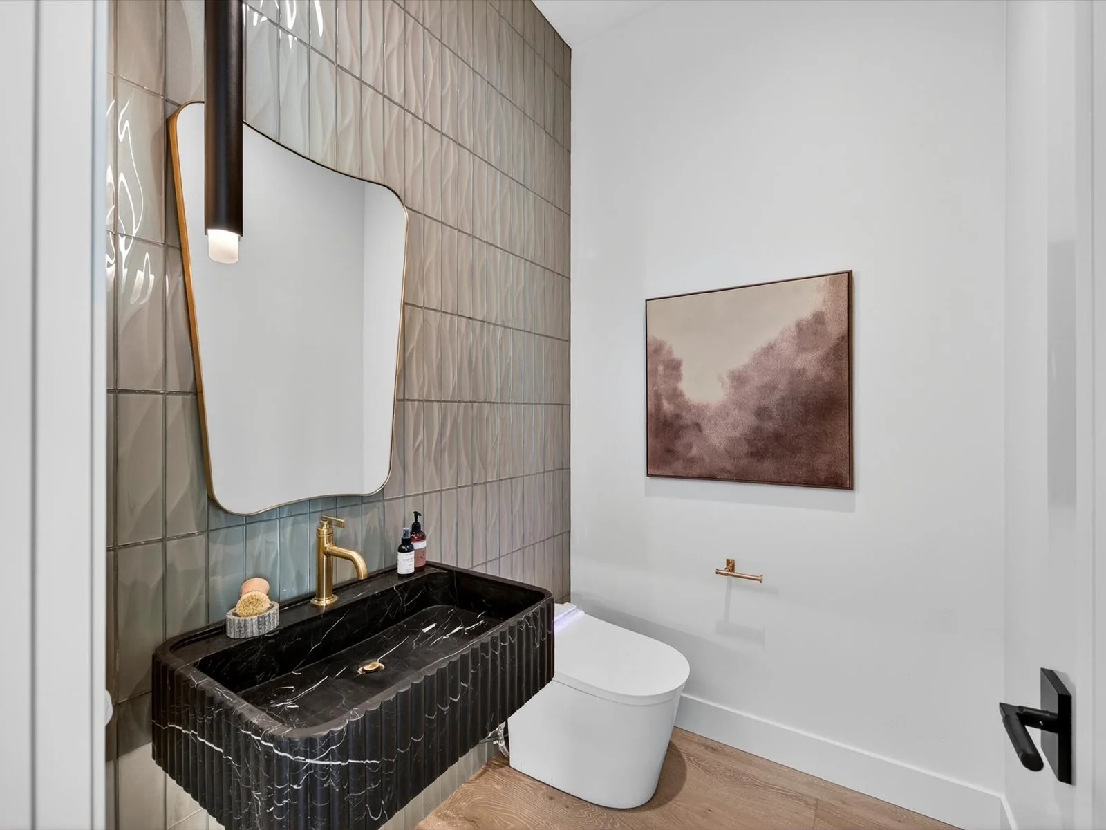Modern bathroom with a black marble rectangular sink, a white toilet, a decorative mirror, a gold-colored faucet, wall art, and minimal decor.