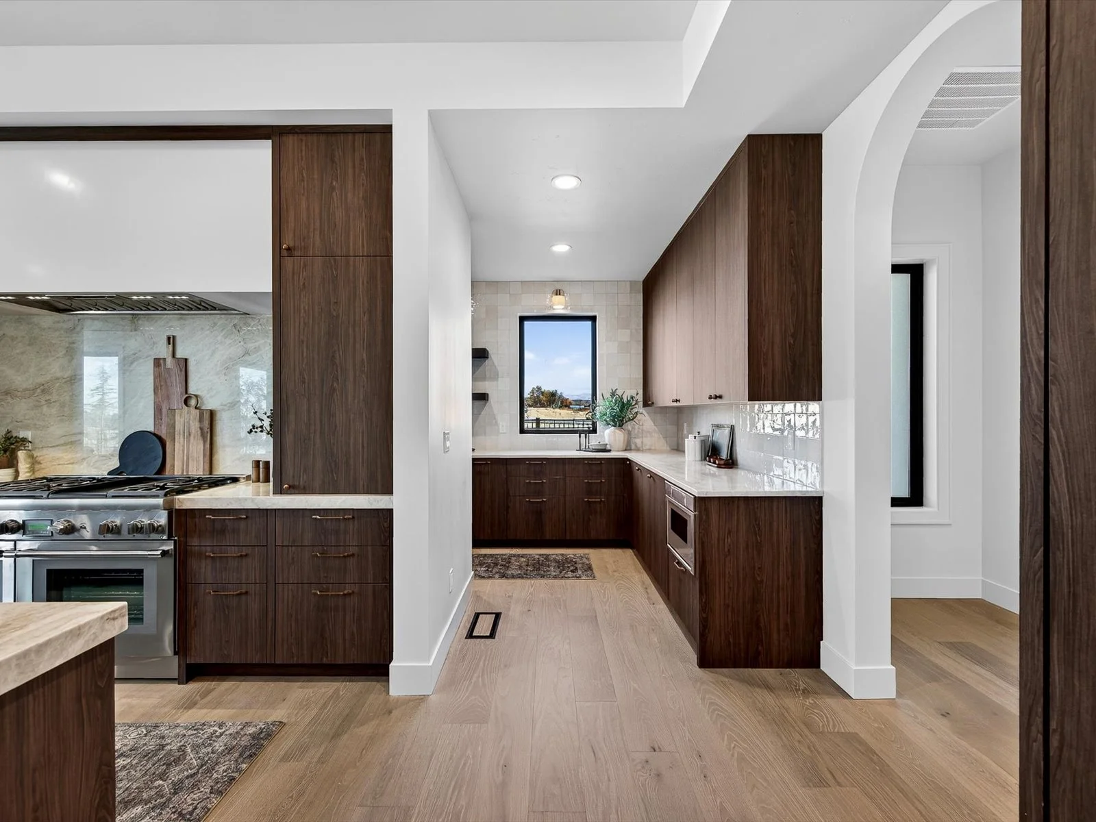 Modern kitchen with dark wooden cabinets, white marble countertops, and a window overlooking the outdoors.