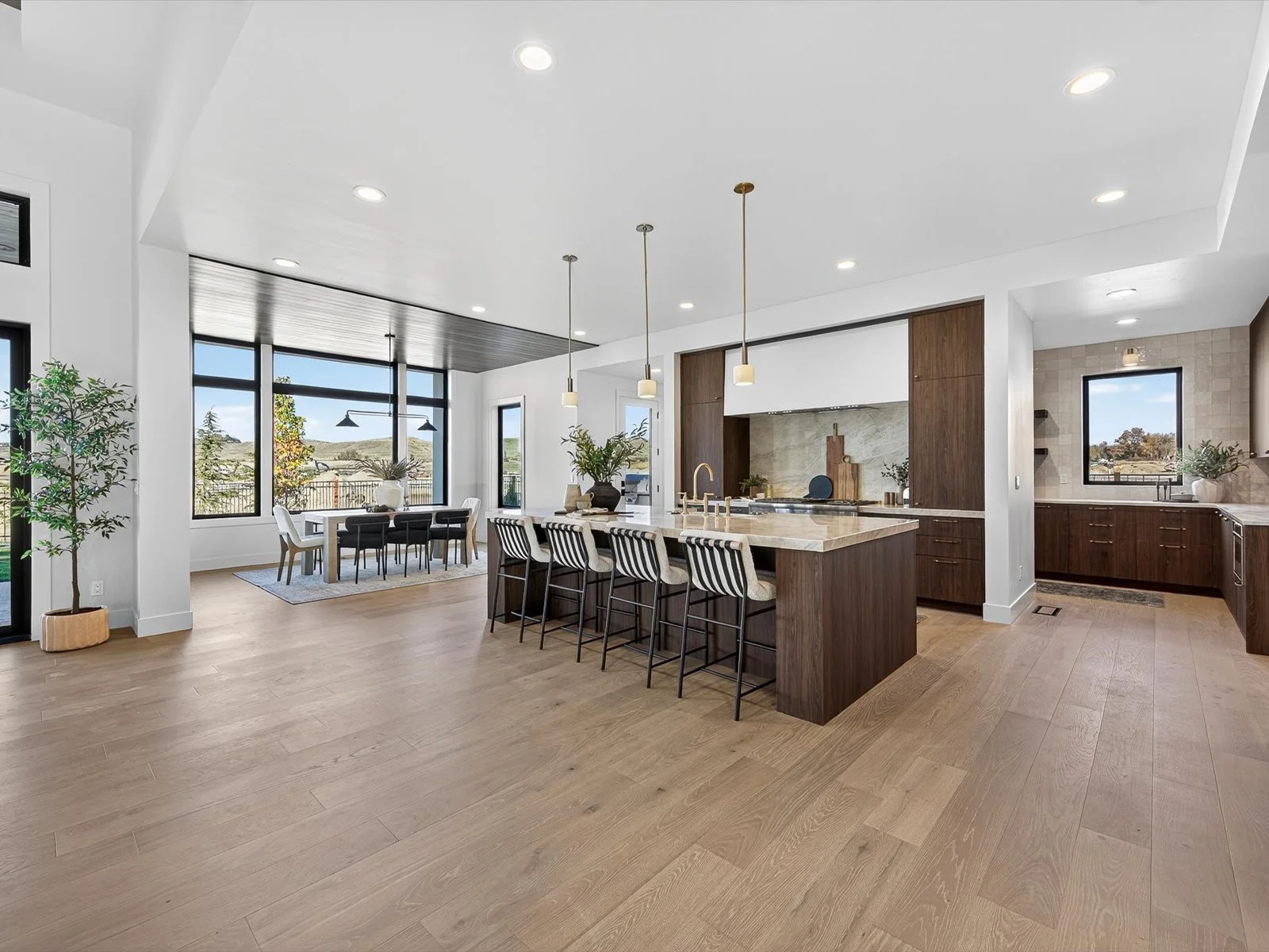 Open-concept kitchen and dining area with large windows, wooden flooring, and modern decor.