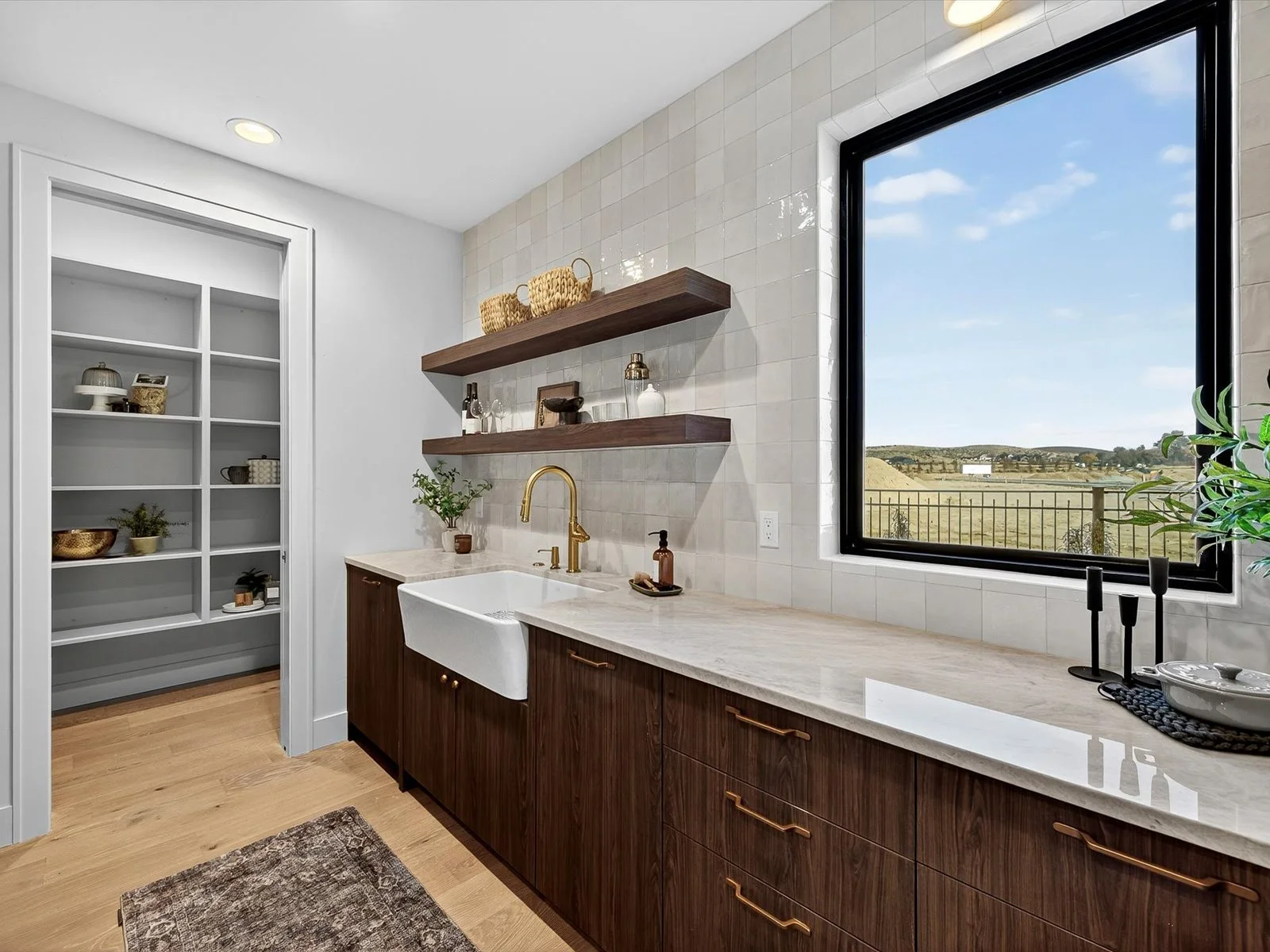 Kitchen with wooden cabinets, a white farmhouse sink, and a large window overlooking a rural landscape.