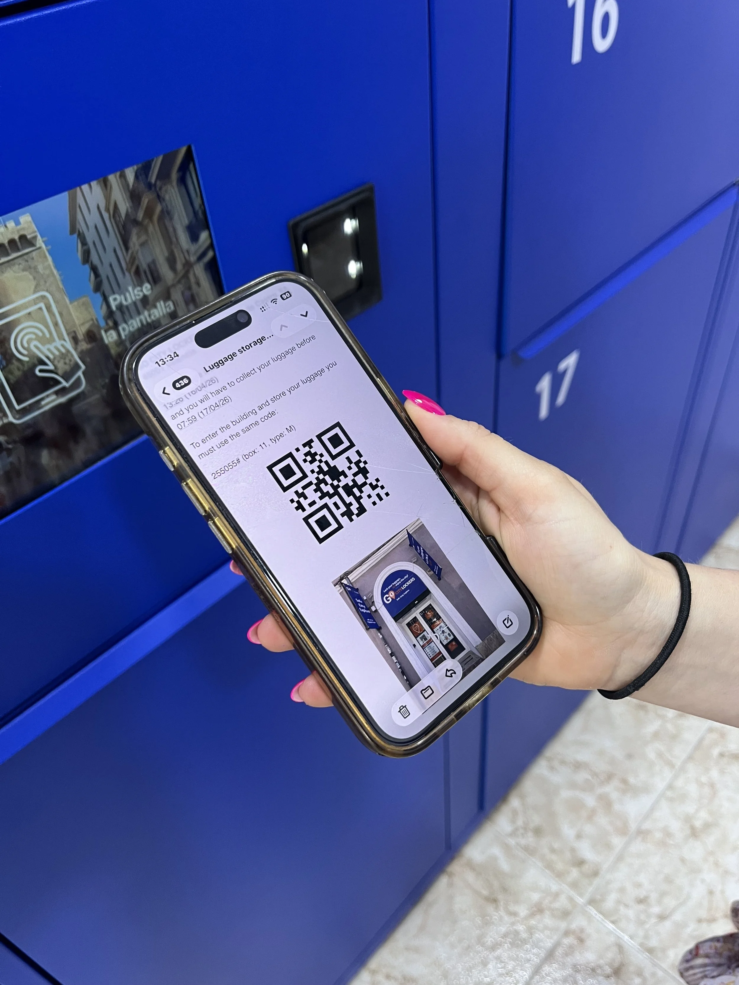 Person holding a smartphone with a QR code displayed on the screen, standing in front of blue lockers numbered 16 and 17.