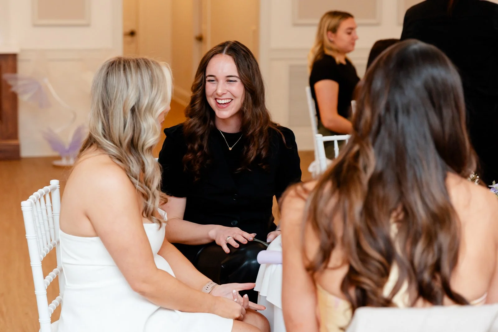 Group of women sitting at a table, smiling and talking at a social gathering indoors.
