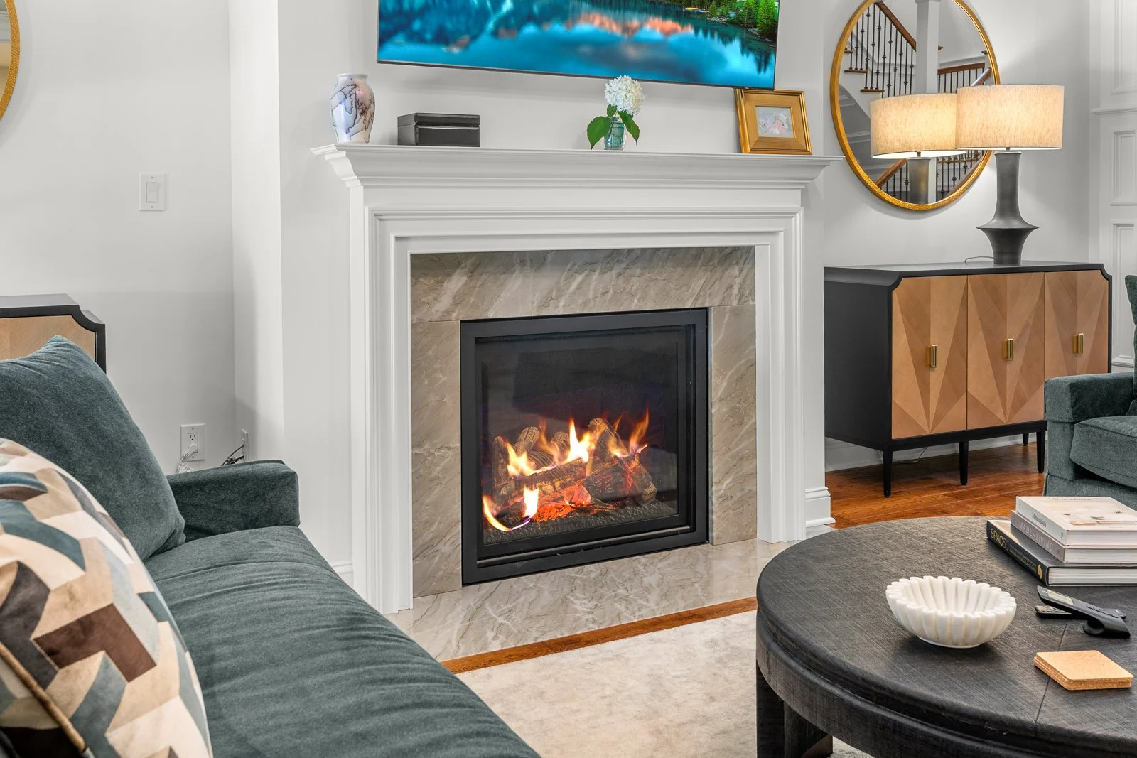 Living room with a fireplace, a gray couch, a black coffee table with a white bowl, and a sideboard with a lamp and mirror