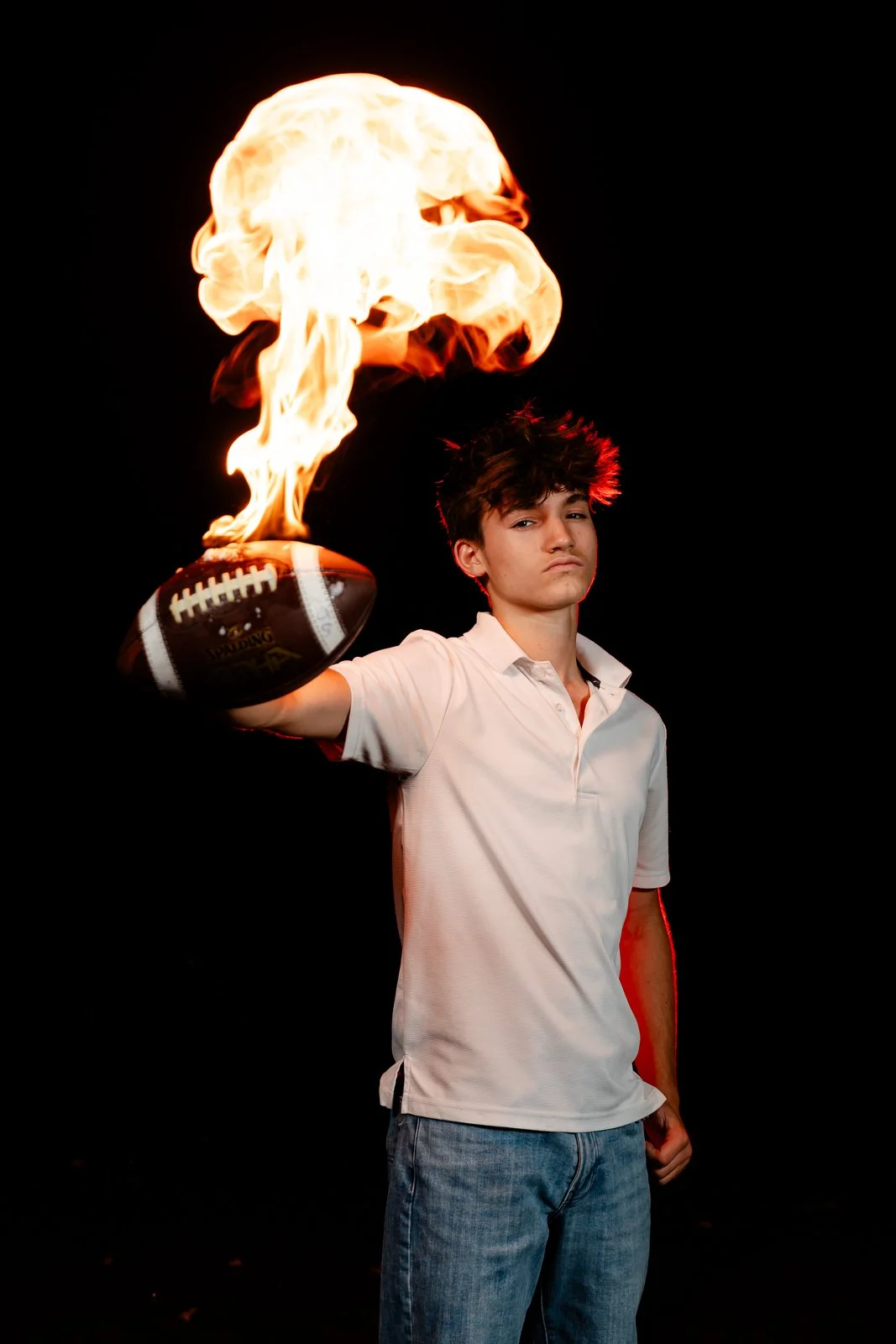 Young man holding a football with a flame creating a fireball above it, against a black background.