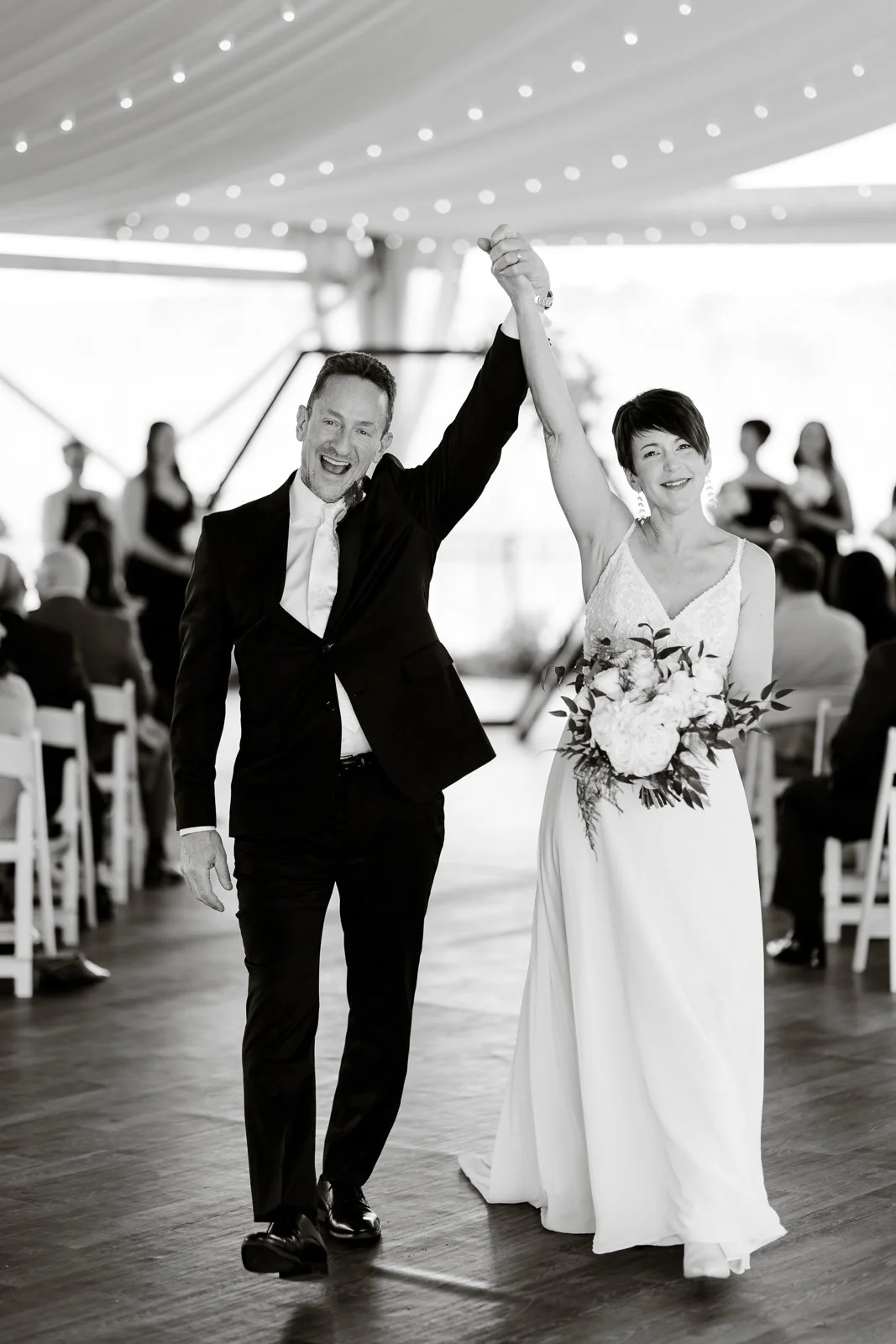 A newlywed couple holding hands and dancing at their wedding reception, smiling and celebrating under a decorated canopy.