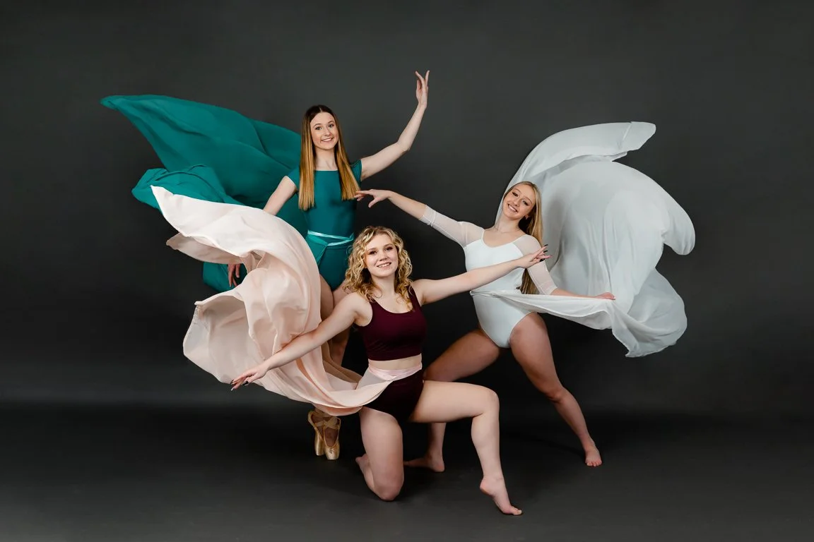 Three women dressed in colorful dance costumes posing against a dark background.