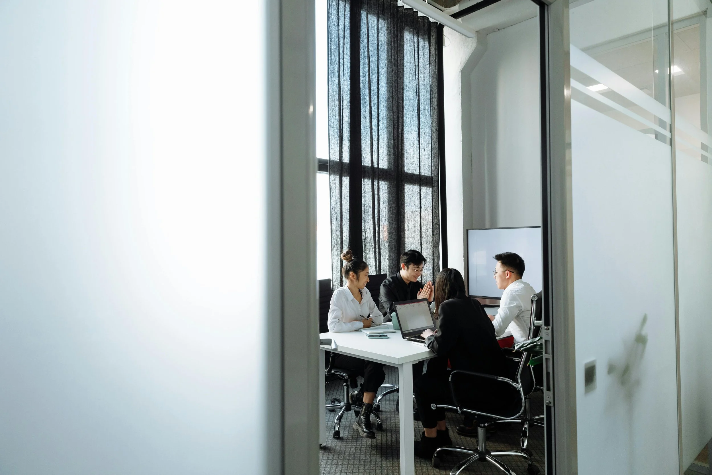 A group of five people in business attire having a meeting around a table in a modern conference room.