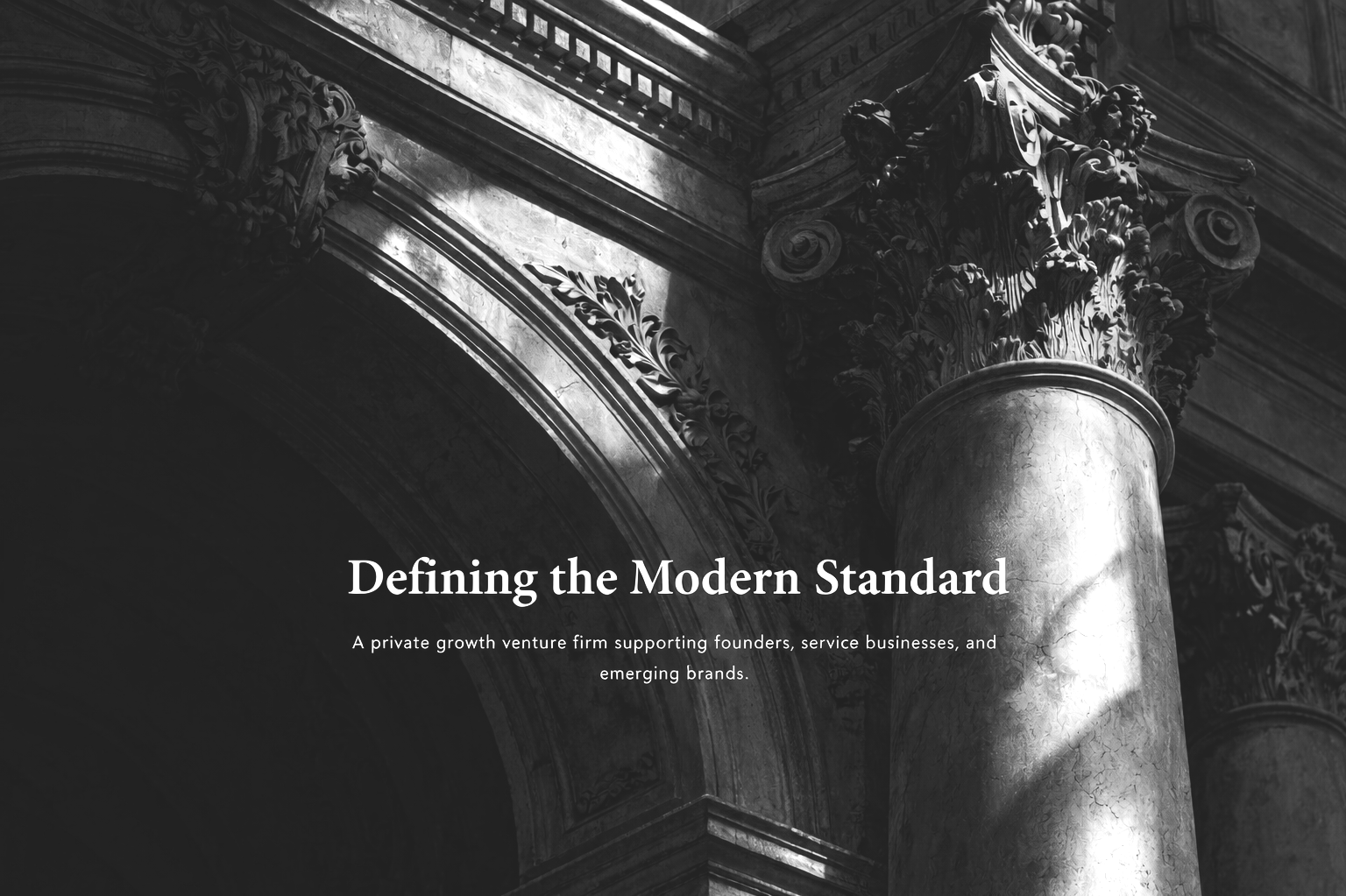 Black and white image of a classical architectural column with intricate carvings on the capital, and a decorative archway above it.