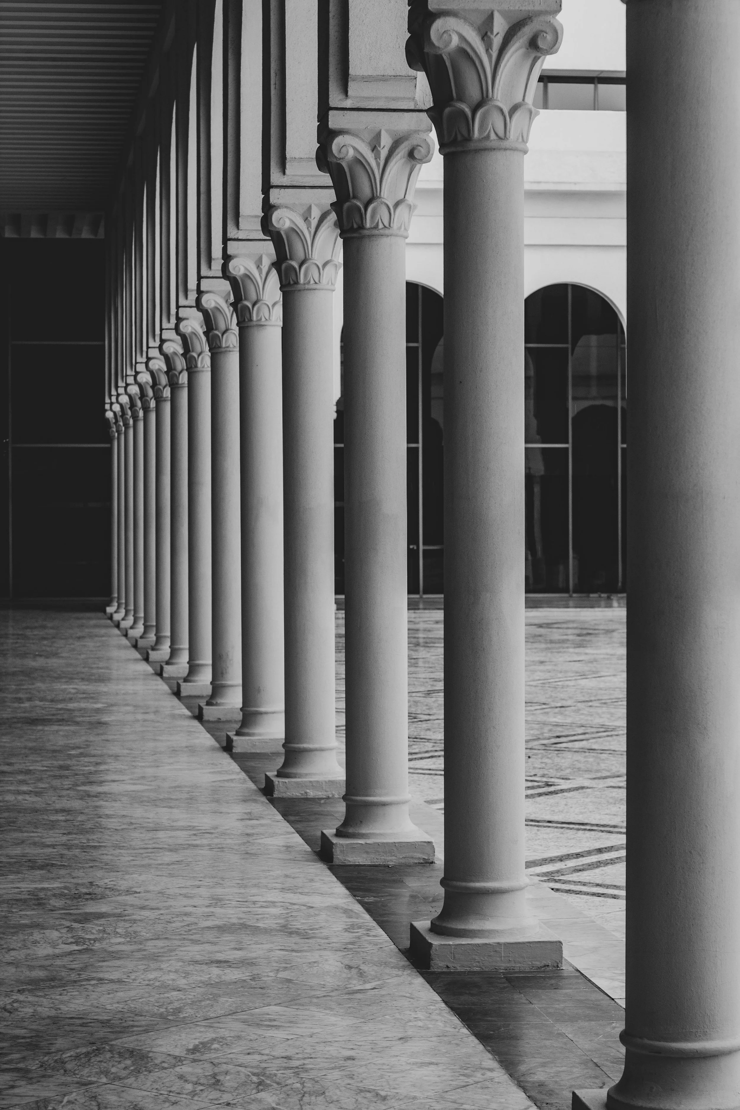A black and white image of classical stone columns supporting a building with arched windows.
