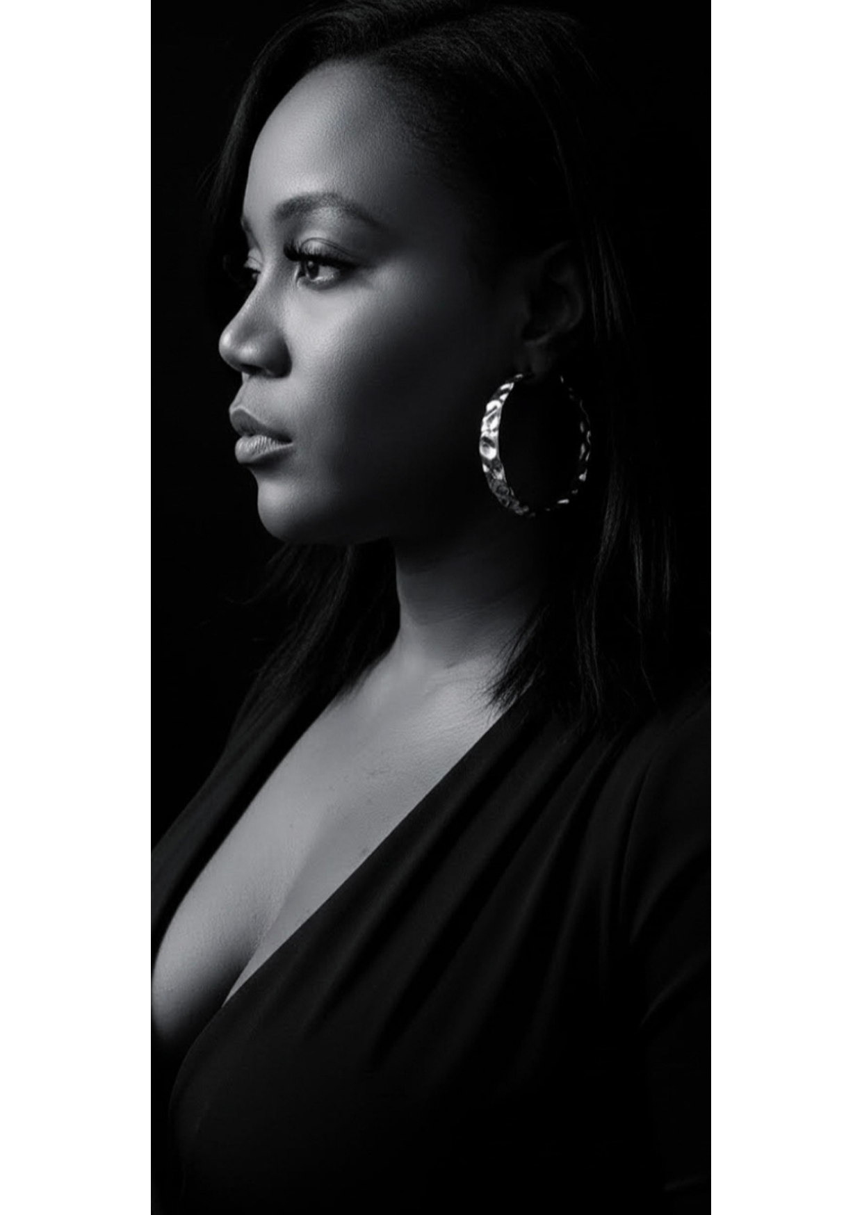 Portrait noir et blanc d'une femme d'apparence africaine, vue de profil, portant de grands boucles d'oreilles et un vêtement sombre, avec un sourire subtil.