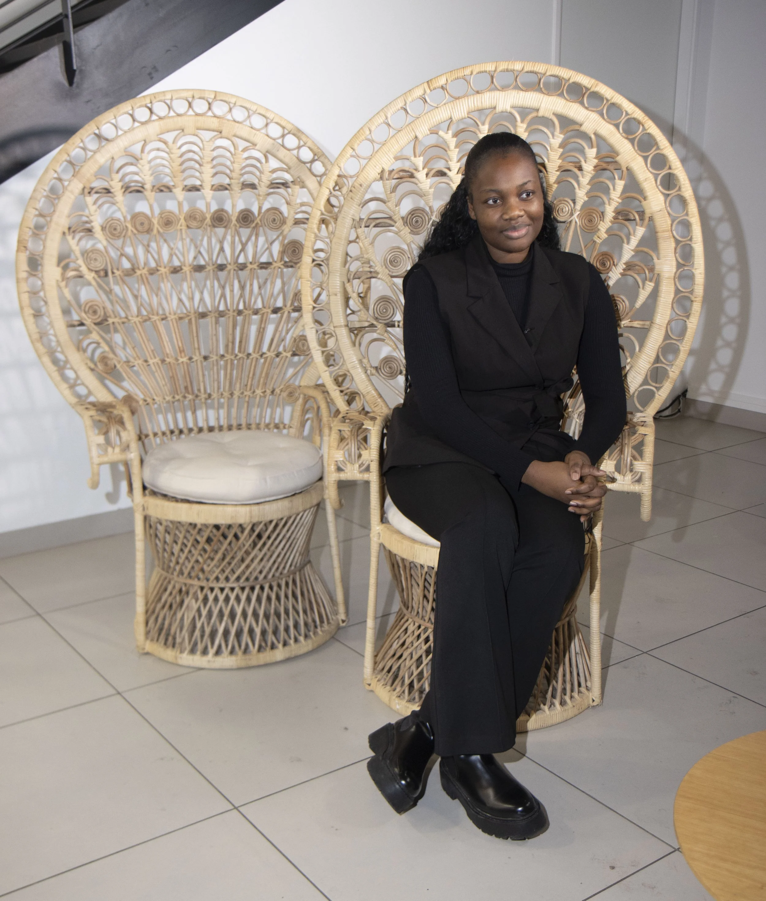 Une femme assise sur une chaise en rotin avec un design de grand cercle, deux chaises en rotin de style similaire derrière elle, dans un intérieur moderne.