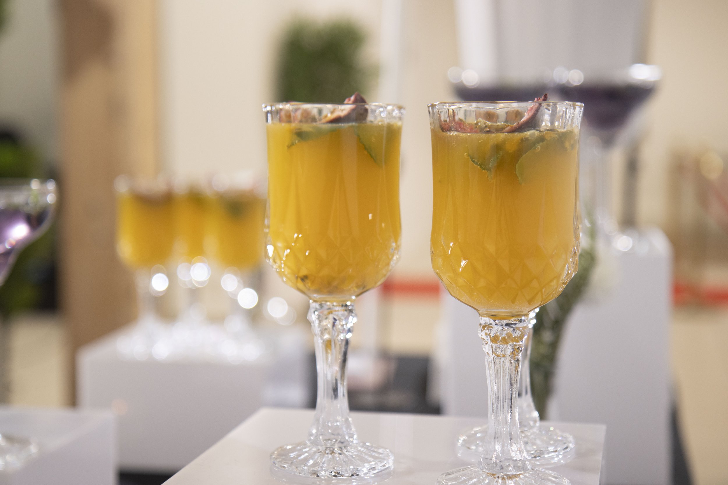 Deux verres ornés de cristaux, remplis d'une boisson jaune-orange avec des feuilles de menthe et des tranches de fruits, probablement un cocktail ou une boisson fruitée, dans un cadre élégant.