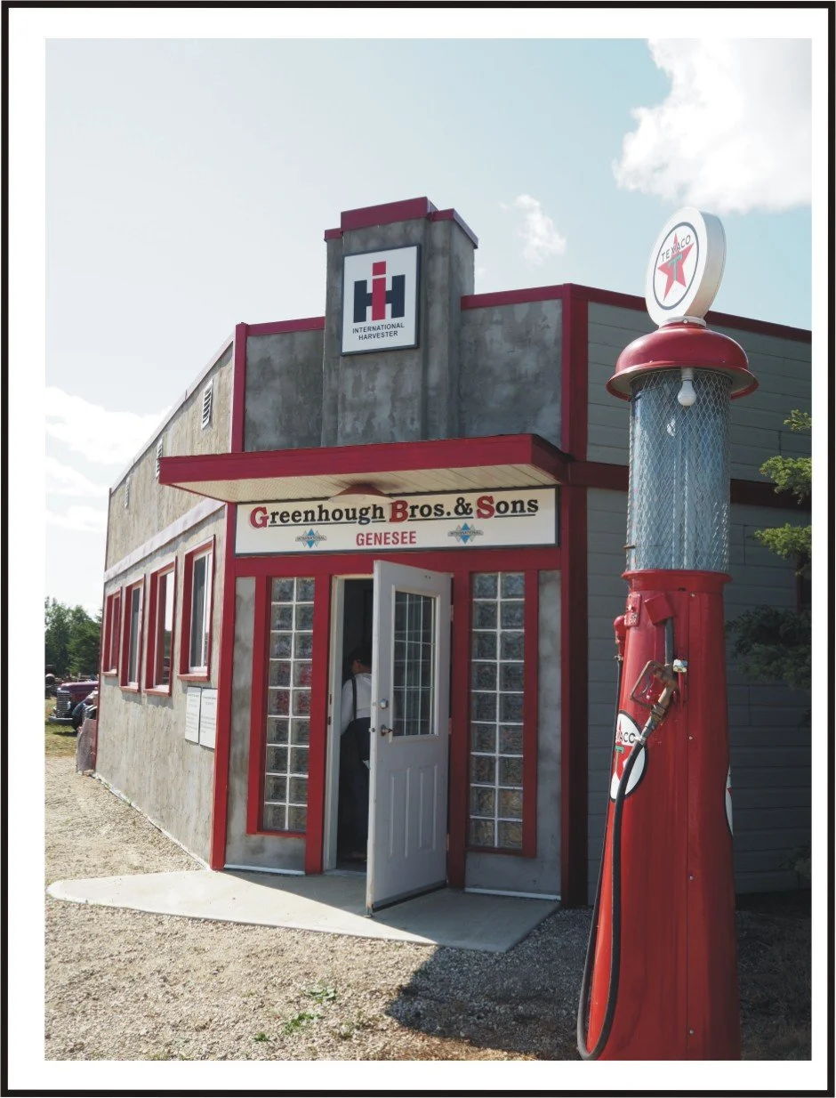 Historic building with a sign reading Greenhough Bros. & Sons, Genesee beer, and a vintage Texaco gas pump outside on a sunny day.