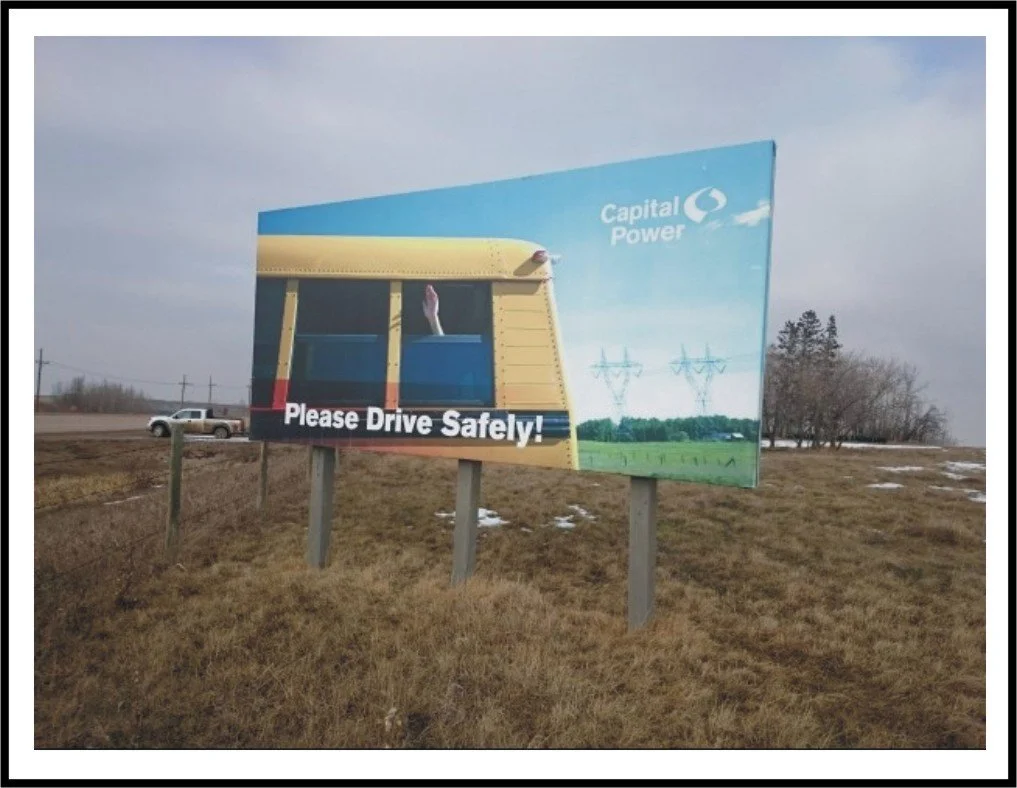 A billboard with an image of a school bus and a hand waving from the window, alongside a power line landscape. The billboard reads 'Please Drive Safely!' and has the Capital Power logo.