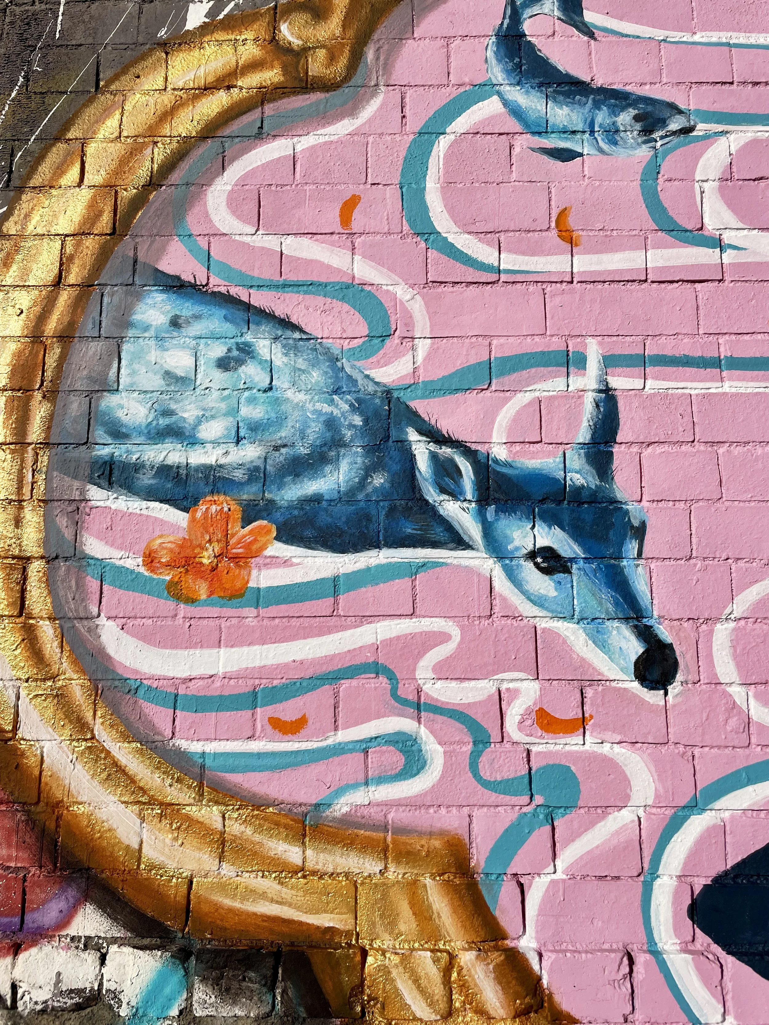 Colorful mural of a blue and white fox with an orange flower on a pink background with swirling white and blue lines and a gold circular border.