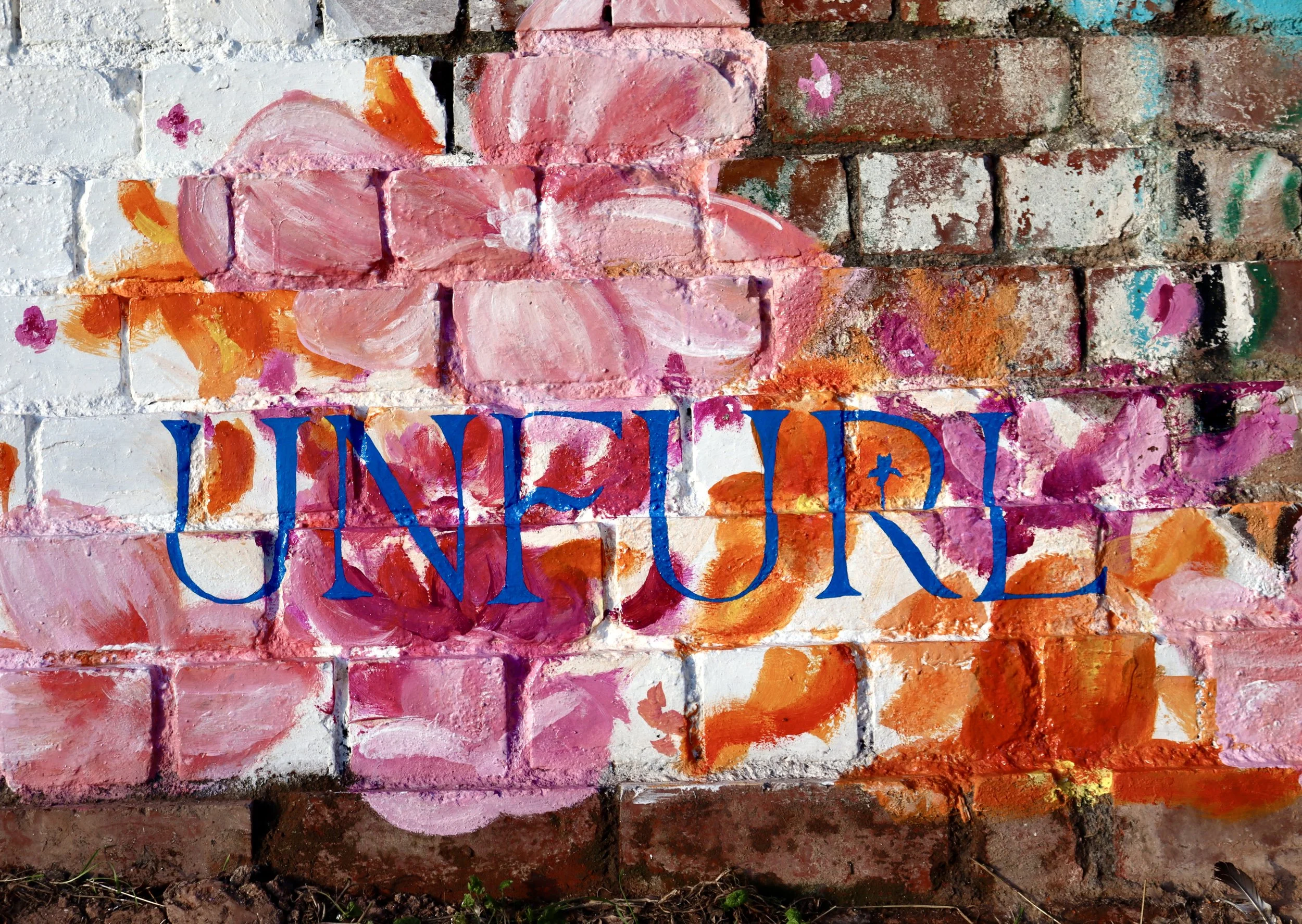 Colorful brick wall mural with pink flowers, orange and purple accents, and the word 'UNIQUE' painted in large blue letters across the center.
